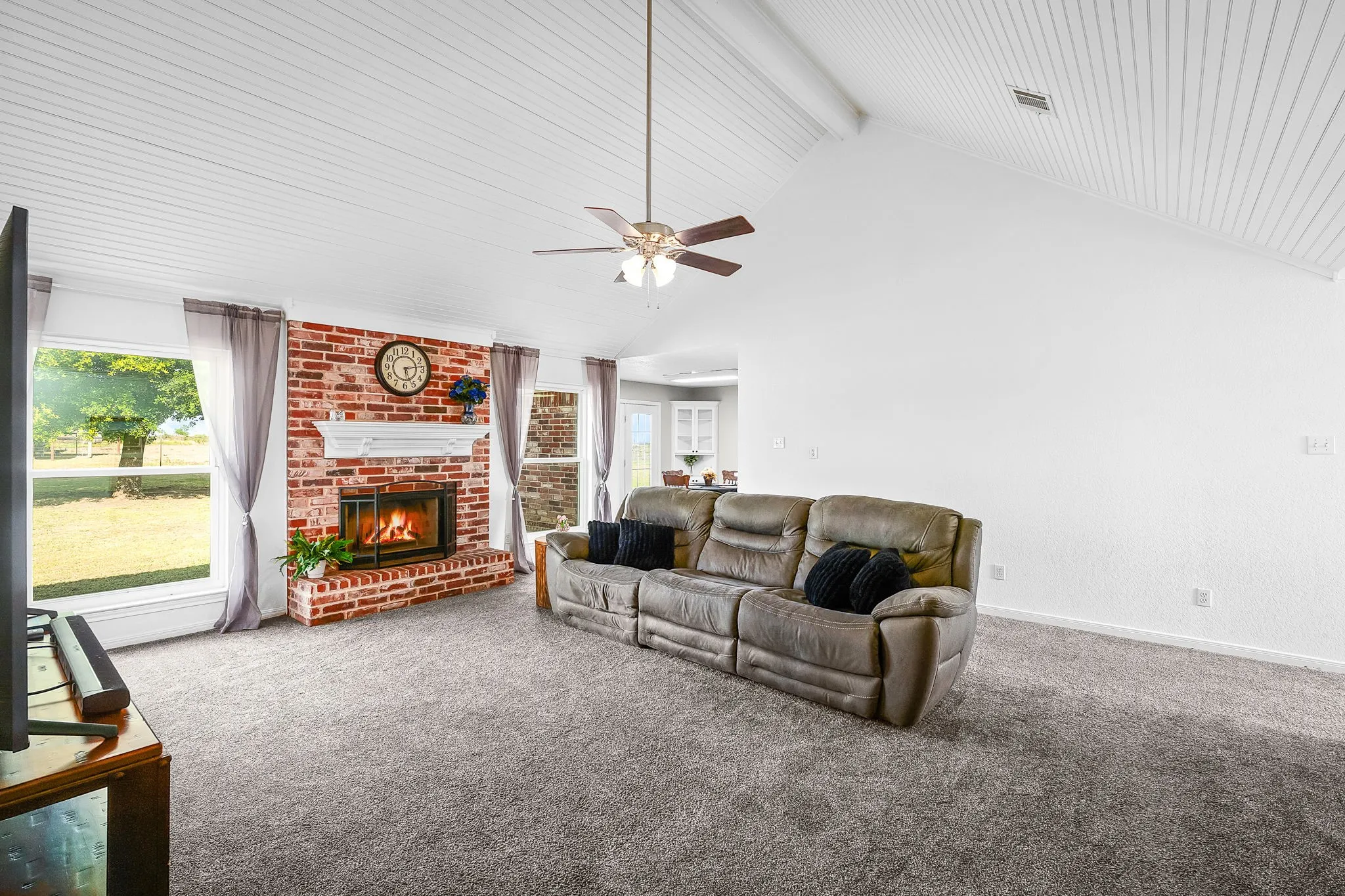 Living area featuring a brick fireplace with a white mantel, vaulted ceilings with wood-finish paneling, and a ceiling fan