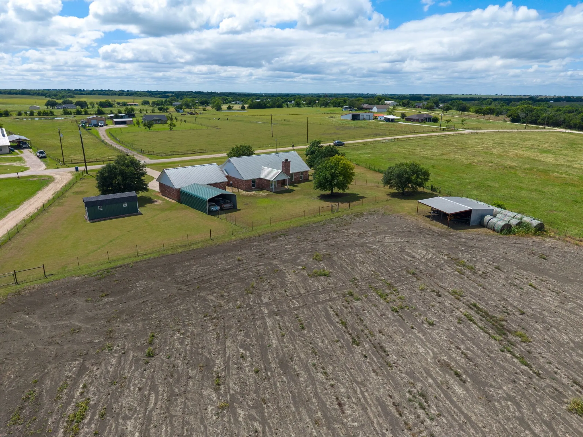 Expansive rural property featuring a brick residence, multiple outbuildings, and a large cultivated field