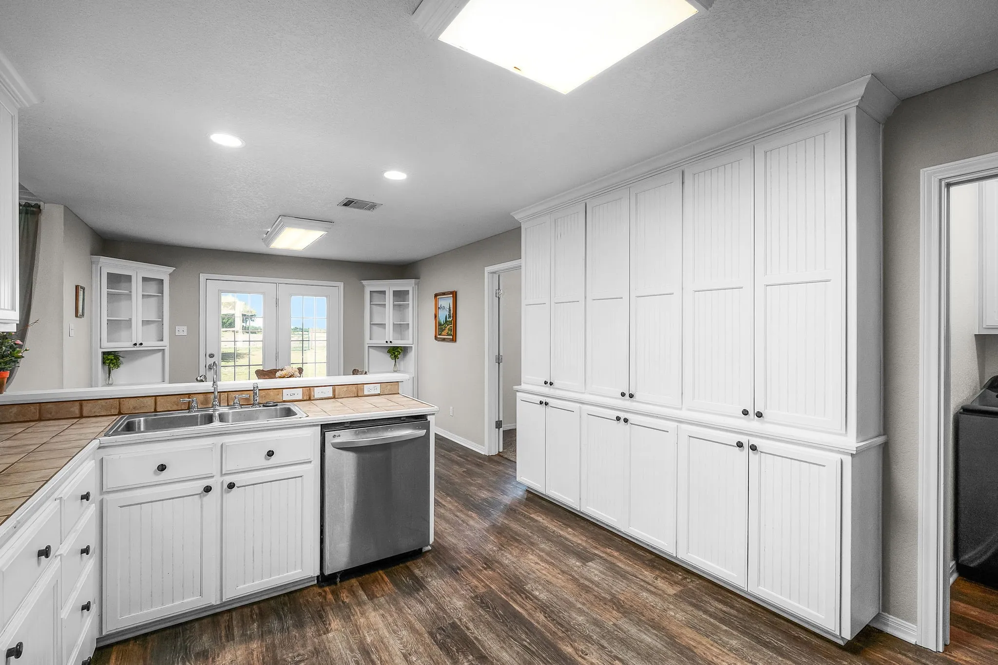 Kitchen featuring extensive white beadboard cabinetry, wood-finish flooring, a stainless steel double basin sink, and a stainless steel dishwasher