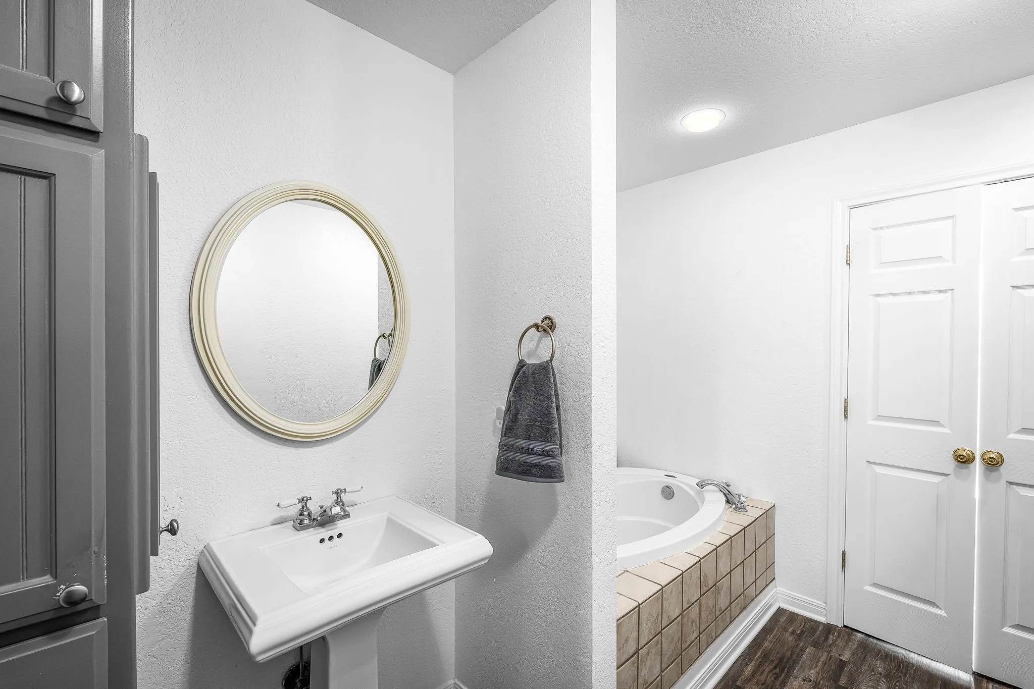 Pedestal sink with chrome fixtures, circular mirror, and built-in cabinetry