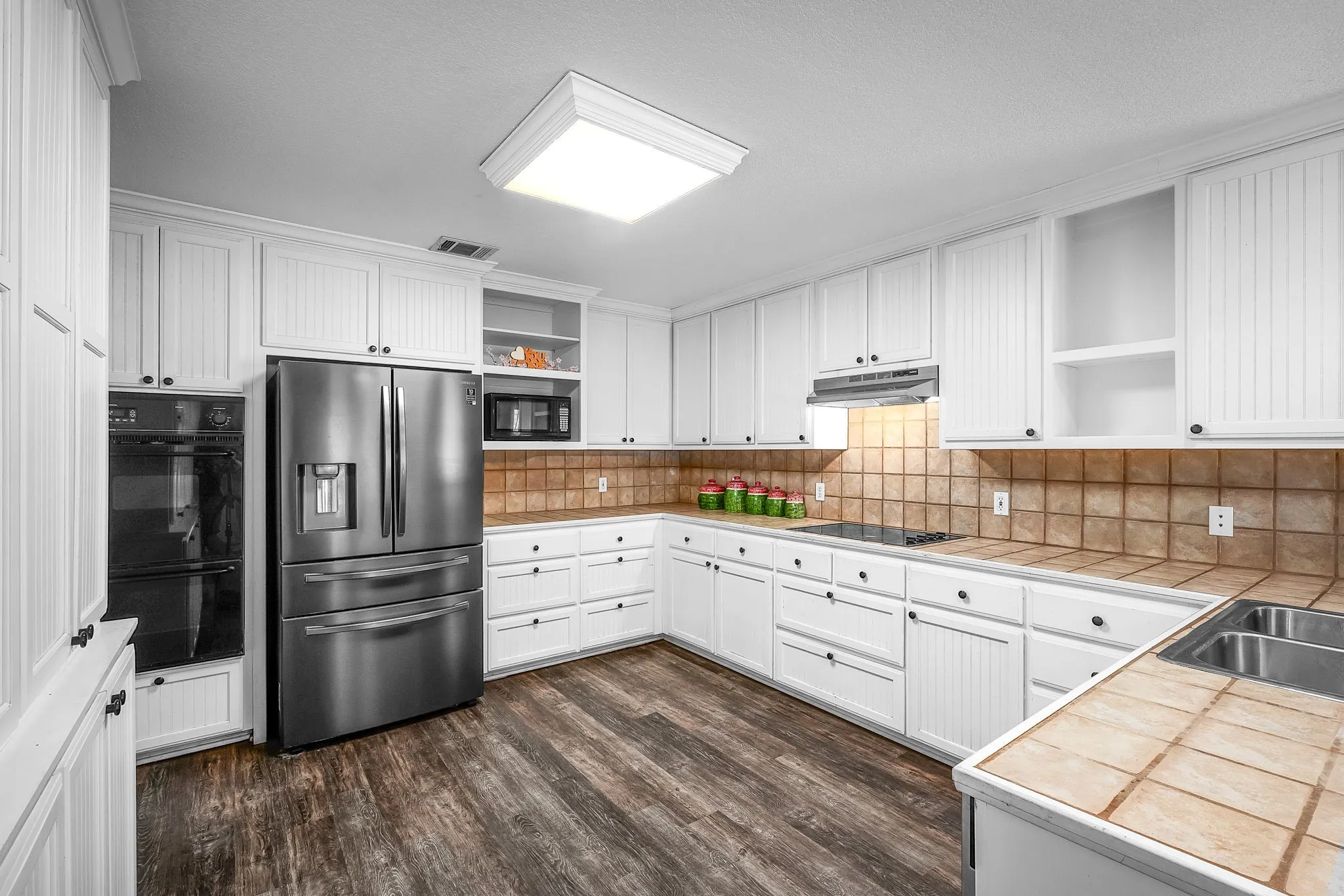 Kitchen featuring abundant white cabinetry, stainless steel appliances, tile countertops, and wood-finish flooring