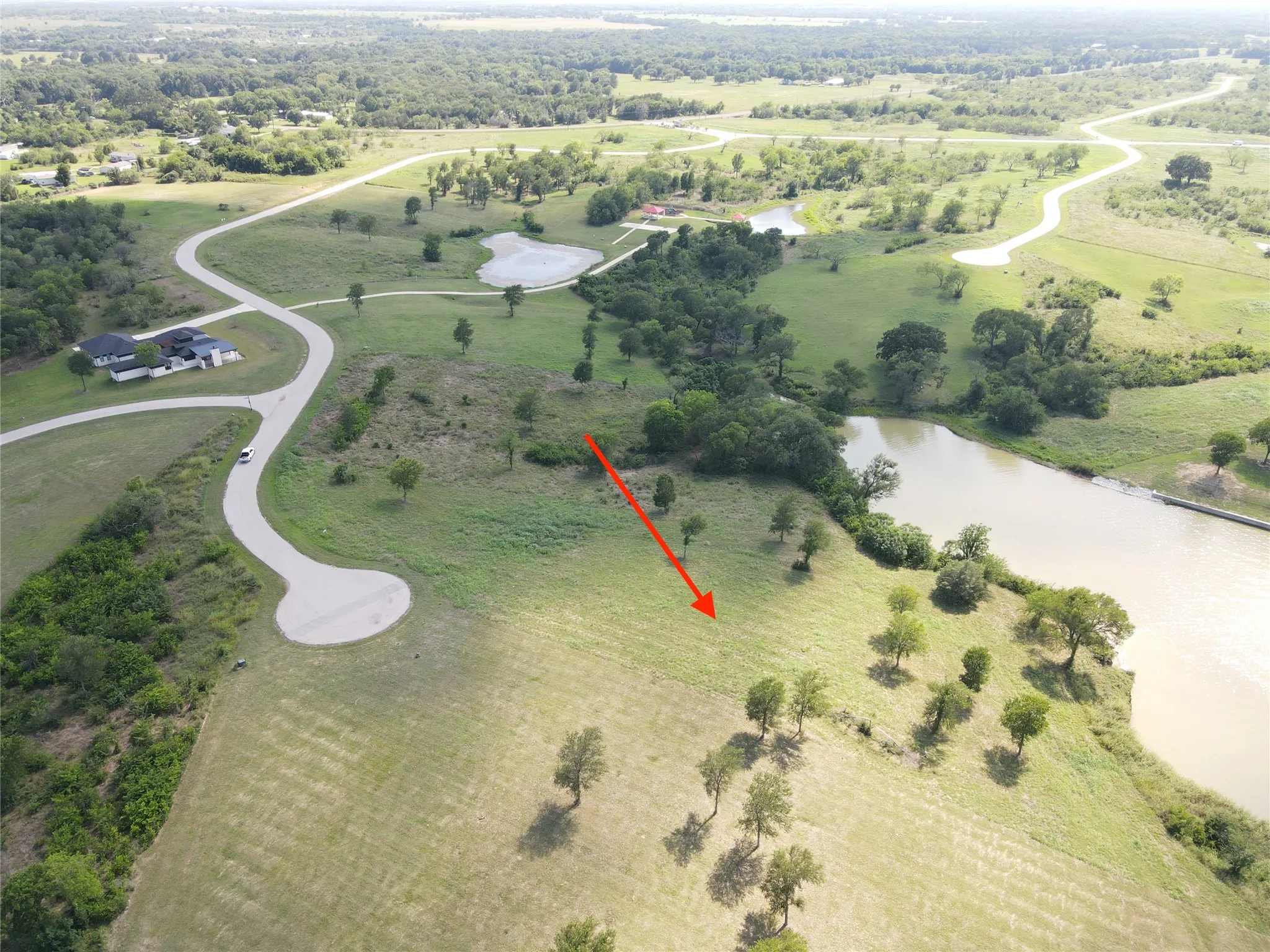 Expansive land parcel featuring a gentle slope, mature trees, and a bordering body of water