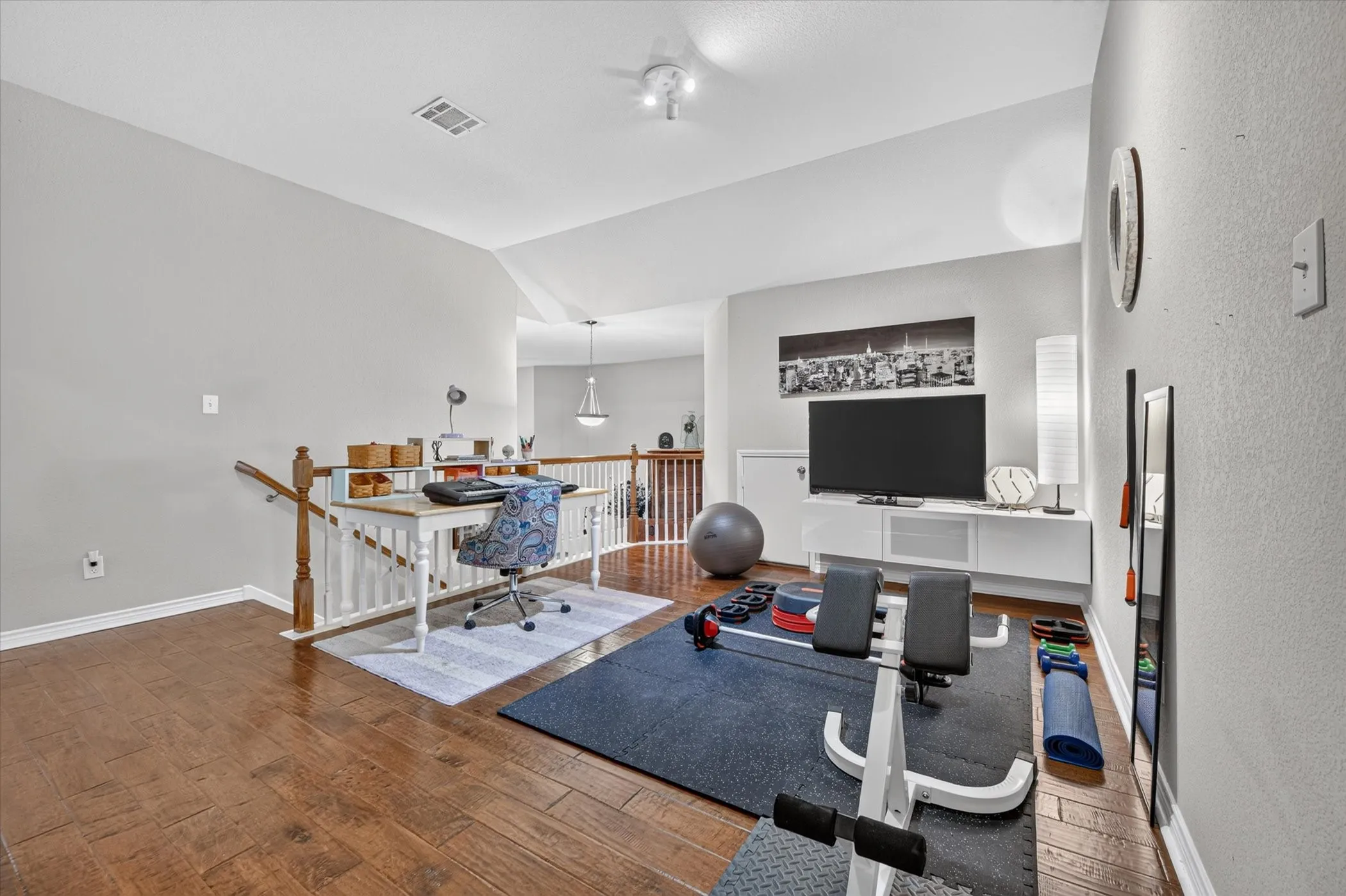 Versatile upper-level space featuring rich wood-finish flooring, a contemporary white media console, and a sturdy white banister