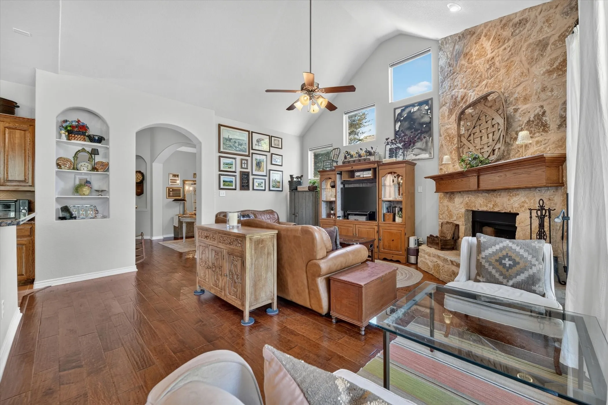 Living area featuring wood-finish flooring, a stone fireplace with a wood mantel, vaulted ceilings, and arched interior doorways