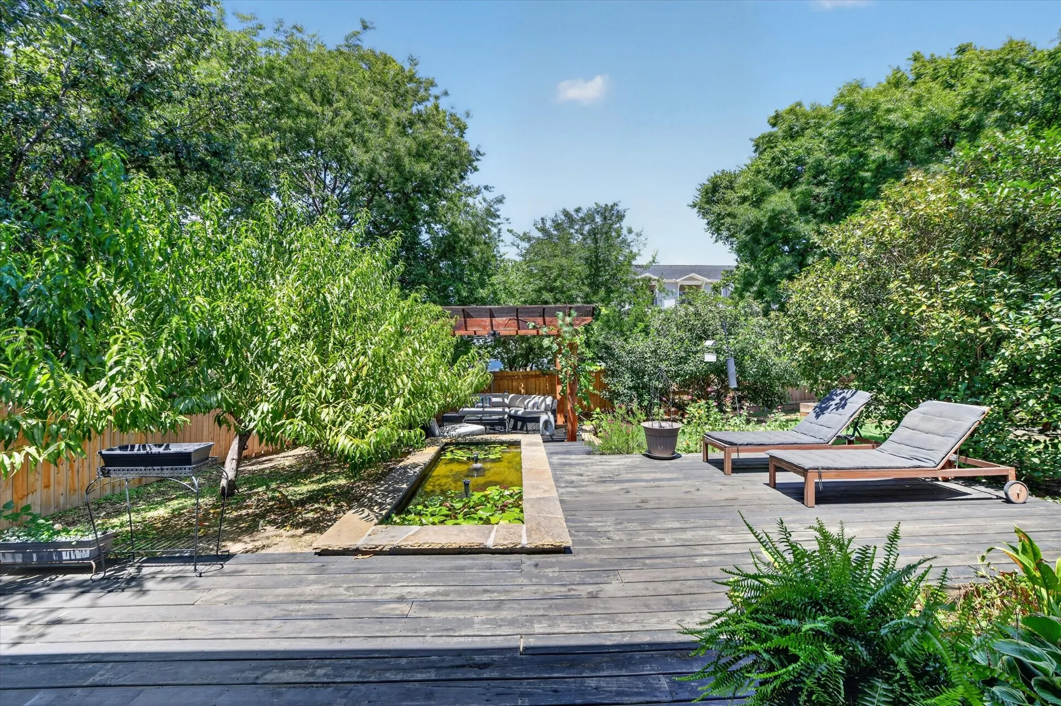 Expansive outdoor deck featuring dark wood-finish flooring, a built-in water feature, and a privacy fence