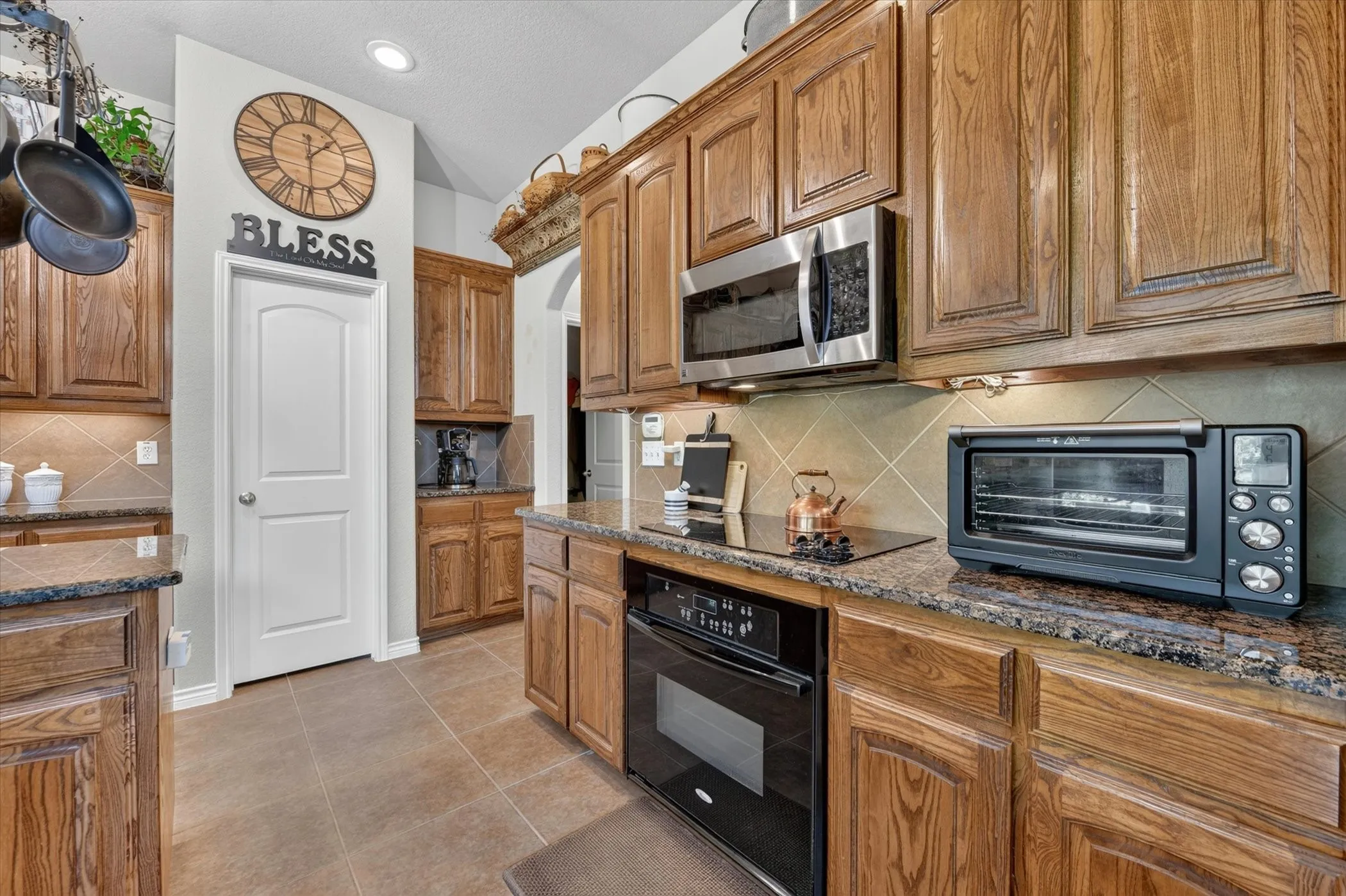 Kitchen featuring wood cabinetry, granite countertops, tile flooring, a built-in oven, and a stainless steel microwave
