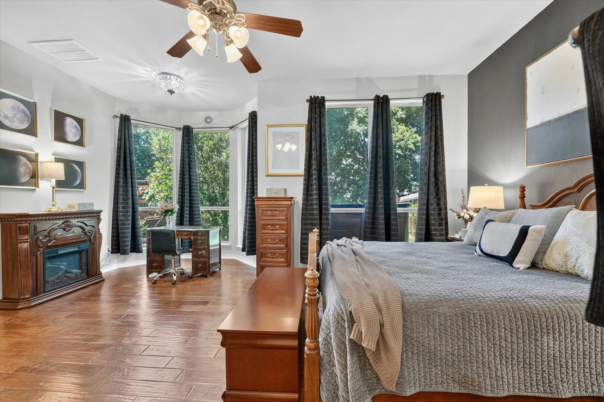 Spacious room featuring wood-finish flooring, a bay window with multiple panes, and a built-in electric fireplace with an ornate mantel