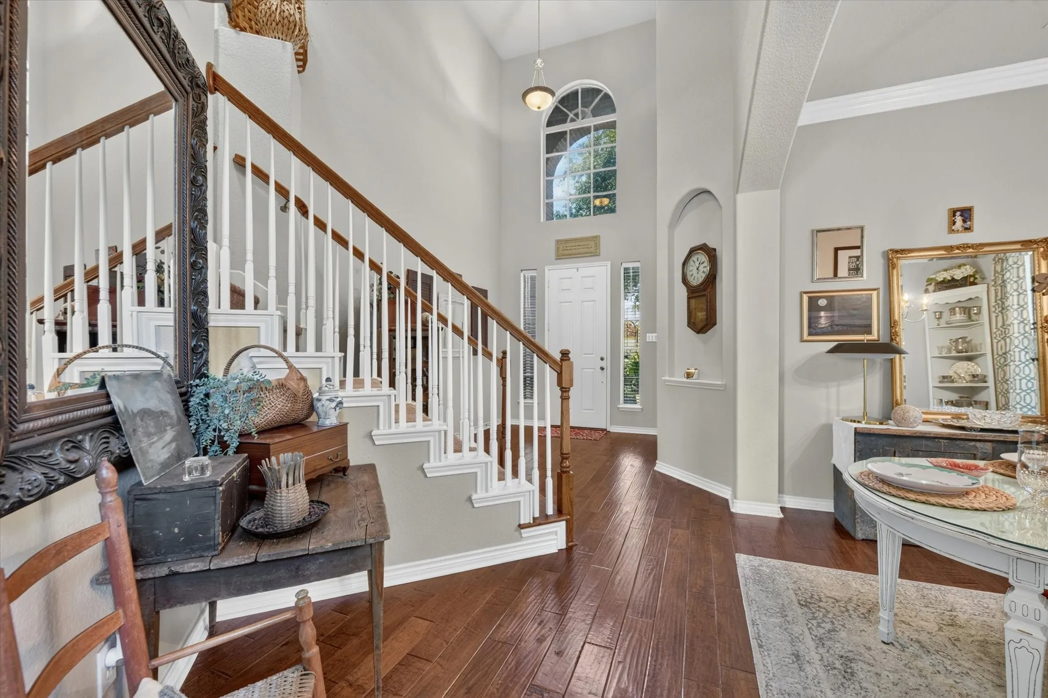 Two-story foyer featuring wood-finish flooring, a white staircase with wood handrails, and a prominent arched window