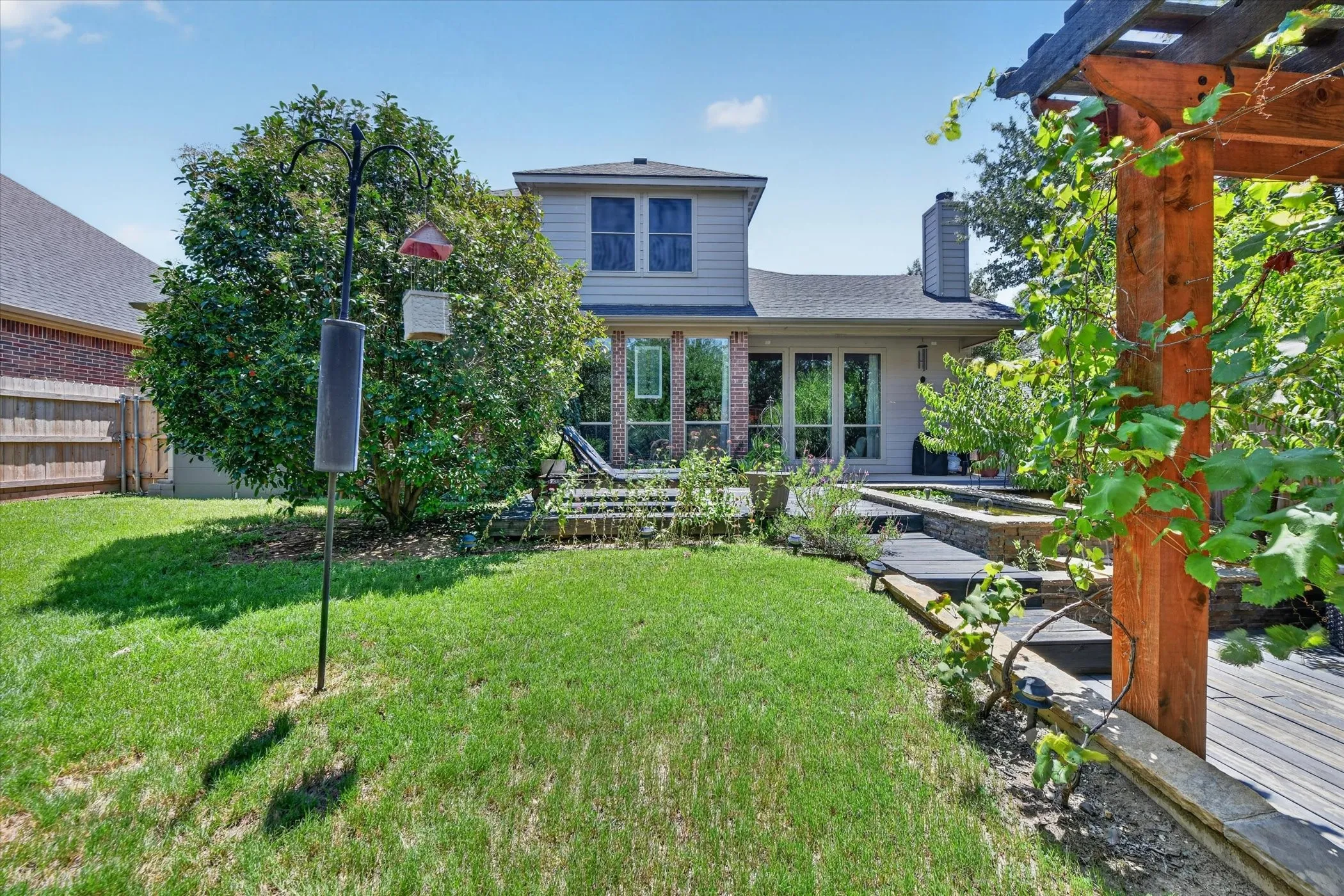 Backyard featuring a wooden pergola, tiered wood-finish decking, and mature landscaping