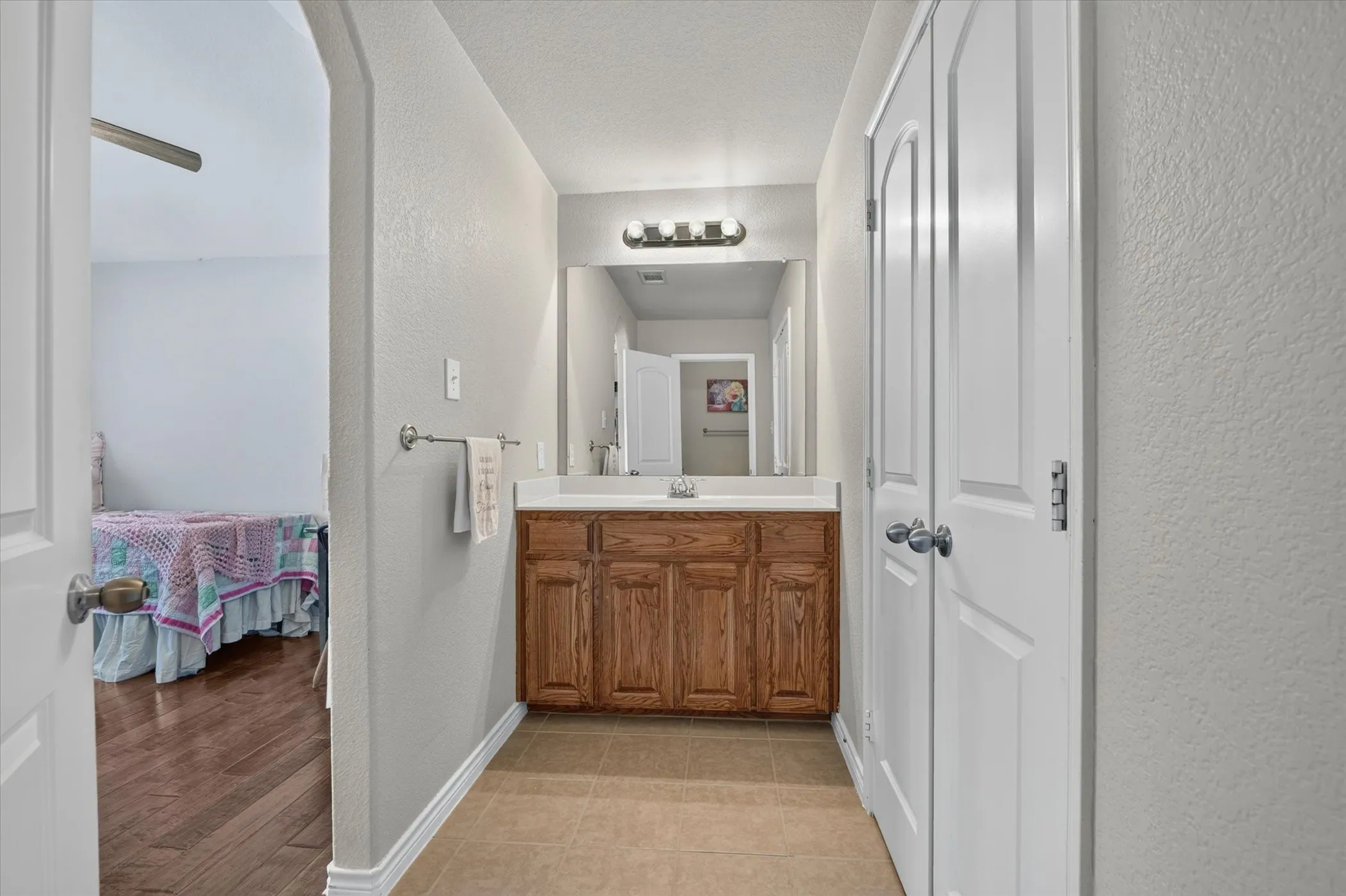 Hallway bathroom featuring a wood-finish vanity with a white countertop and a mirror with overhead lighting