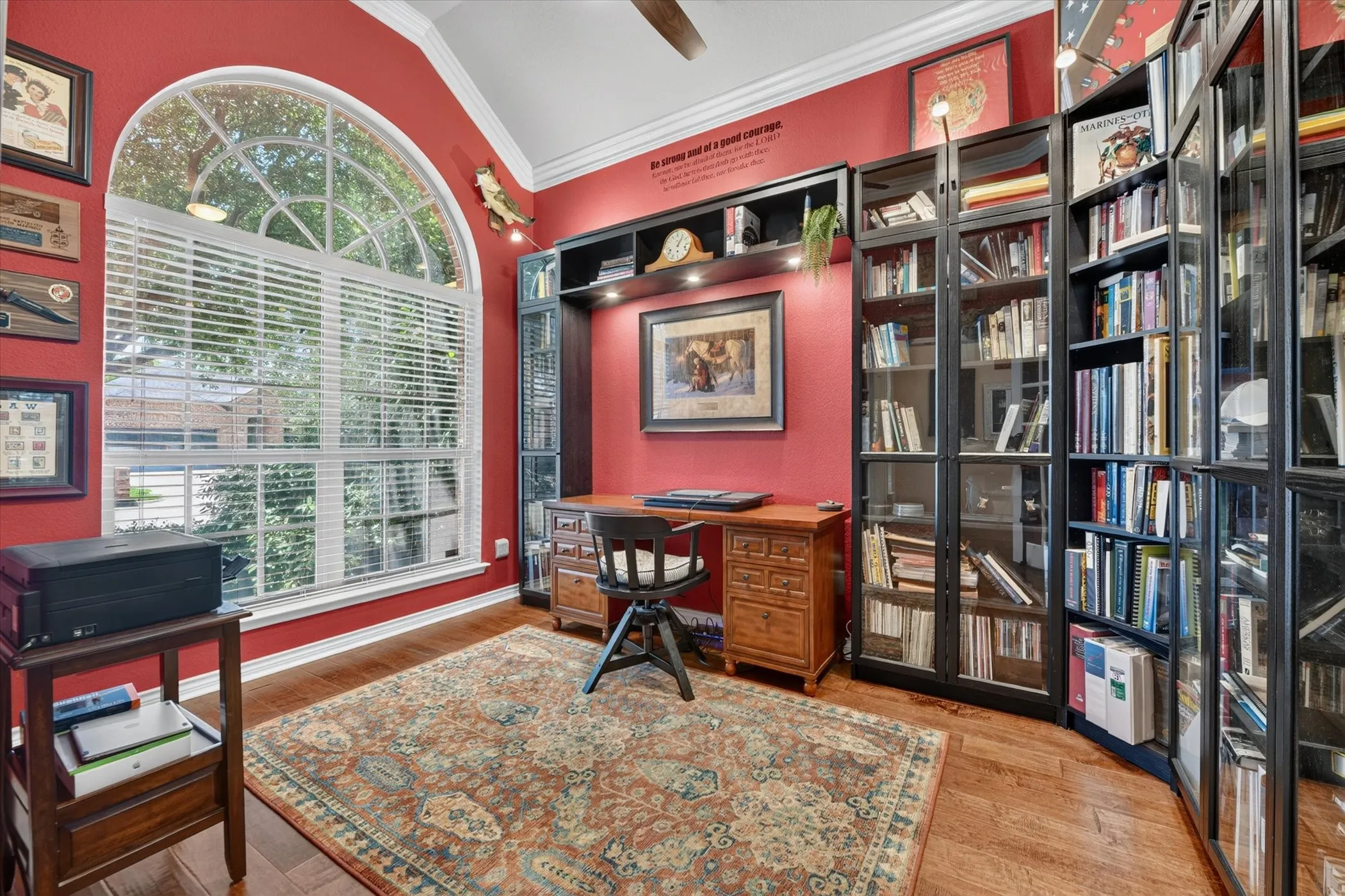 Room featuring a large arched window with blinds, wood-finish flooring, and built-in shelving units