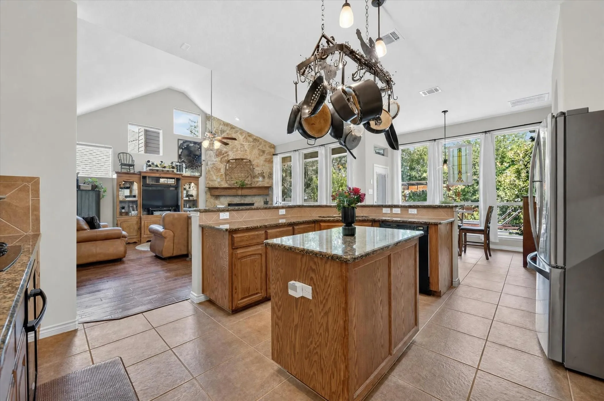 Kitchen featuring a central island with a granite countertop, tile flooring, wood cabinetry, and stainless steel appliances