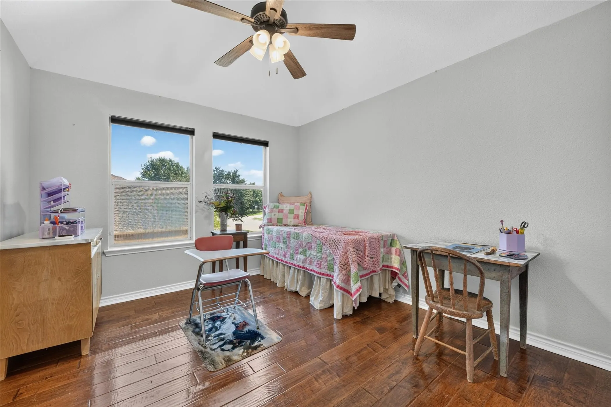 Bright room featuring wood-finish flooring, two large windows, a ceiling fan with light fixture, and light-toned wall paint