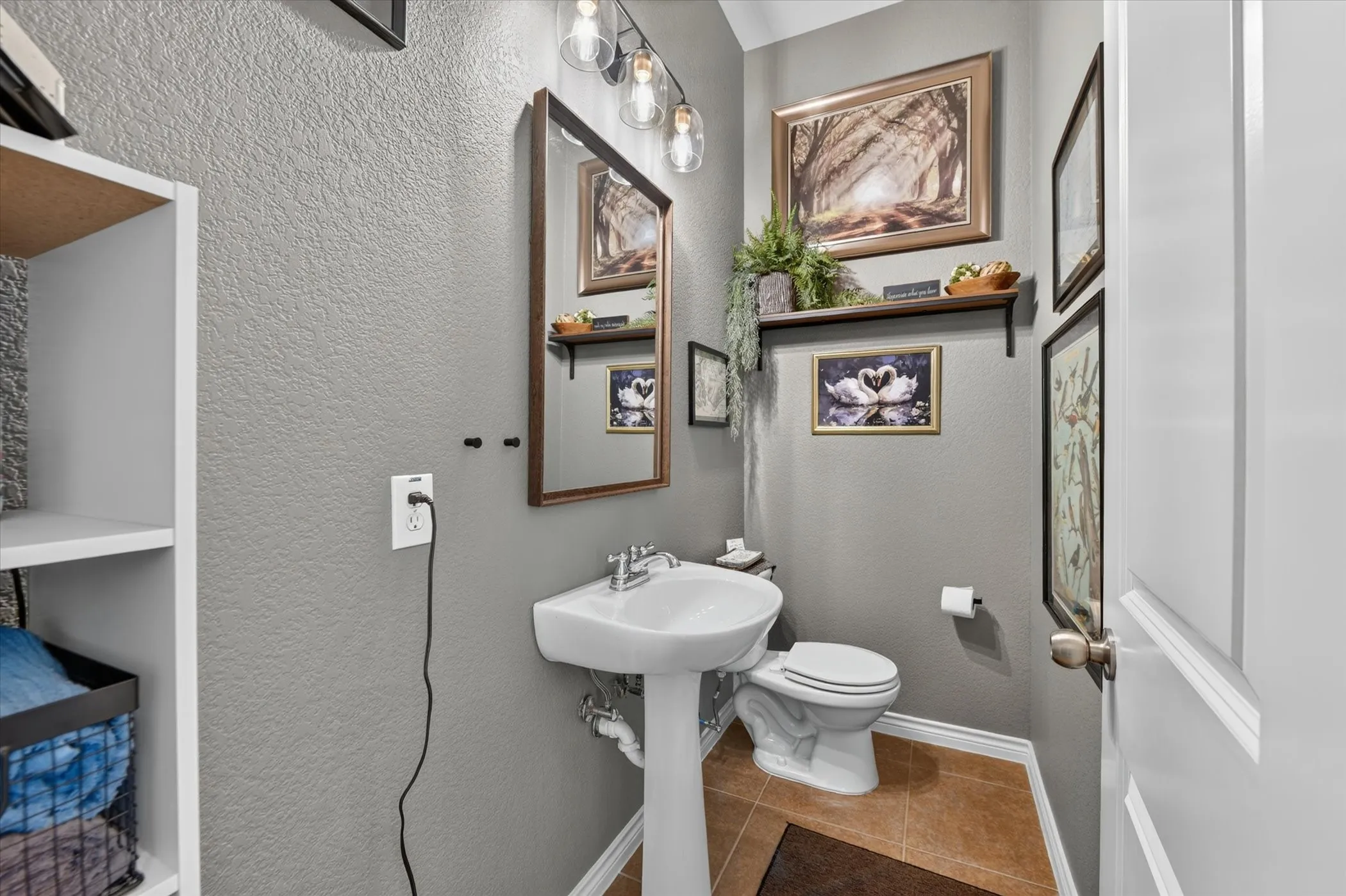 Half bathroom with pedestal sink with chrome fixtures, coordinating toilet, wood-frame mirror, and ceramic tile flooring