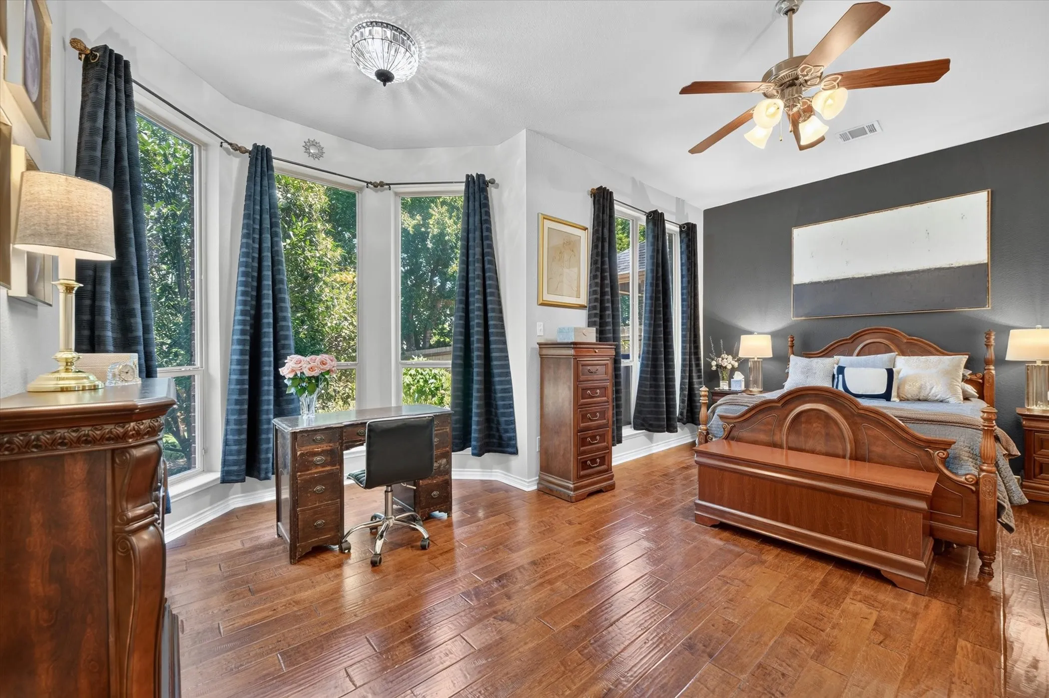 Hardwood flooring throughout this spacious room, featuring a bay window with ample natural light, a ceiling fan with integrated lighting, and a contemporary light fixture