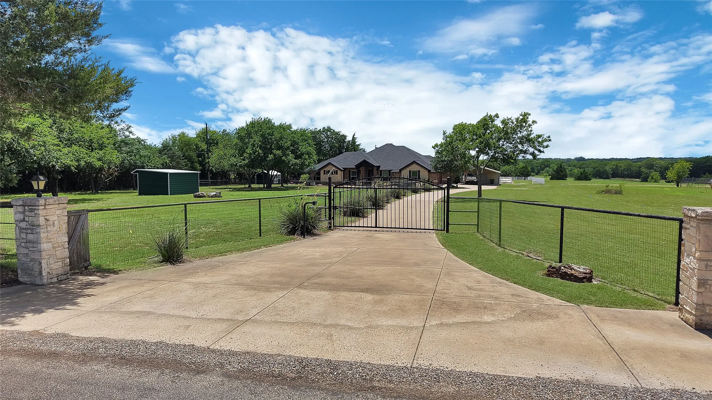 Private gated entrance leads down a long driveway with pipe top rail fence