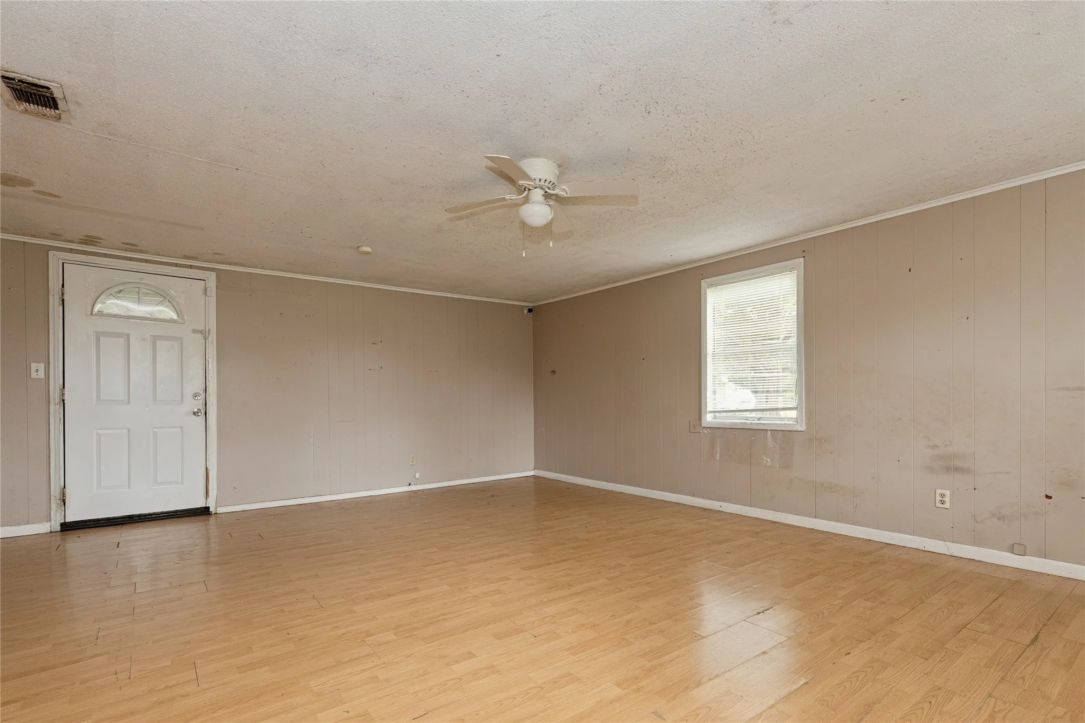 Spacious room featuring wood-finish flooring, a ceiling fan, and a paneled entry door with an arched window