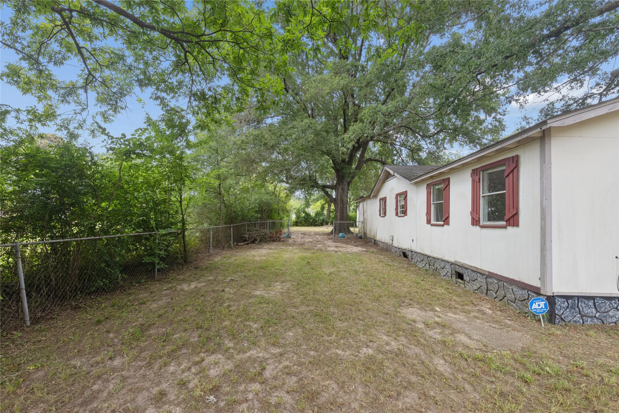 Side exterior featuring light-colored siding, red louvered shutters, and a dark-toned stone-patterned foundation
