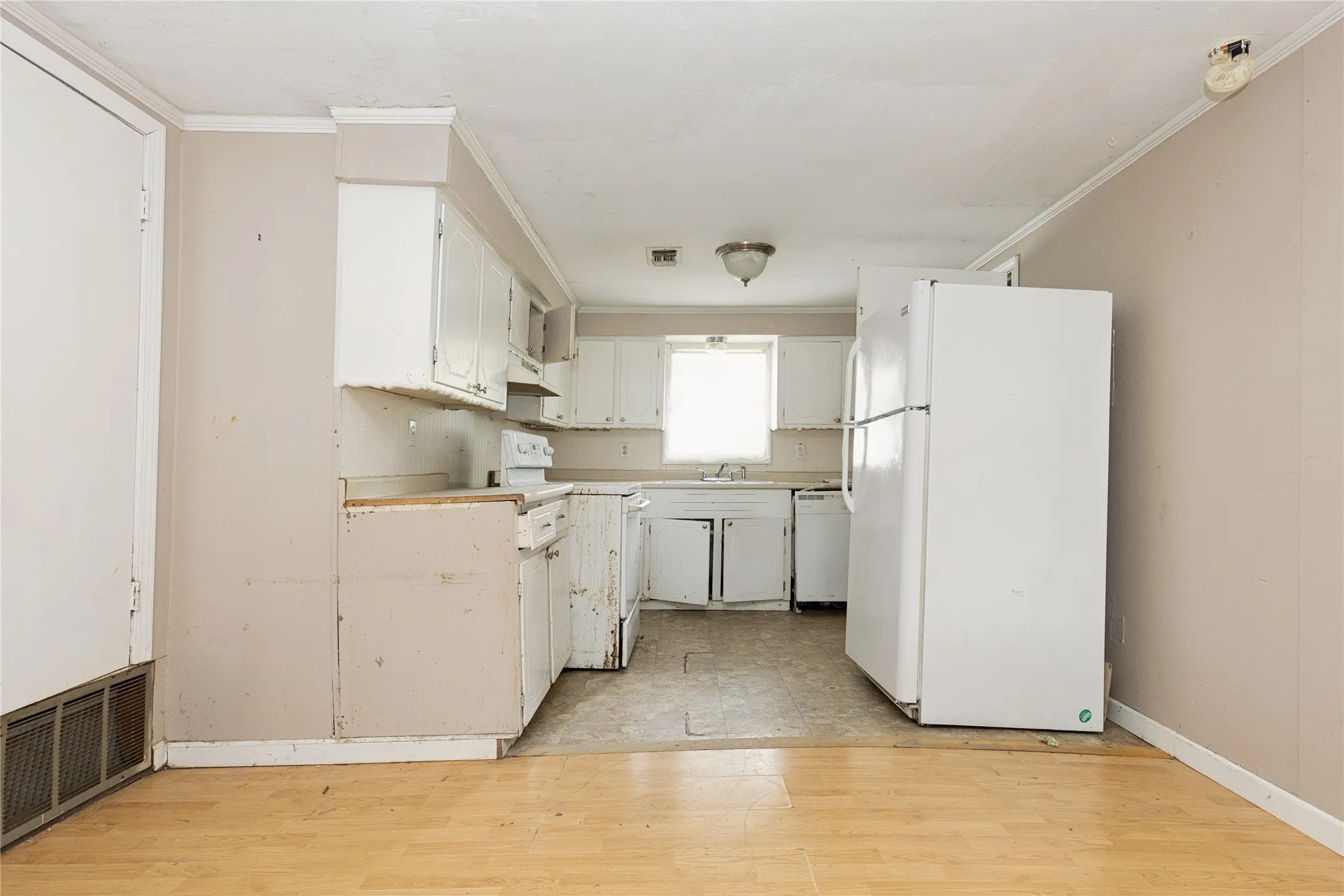 Kitchen area featuring white cabinetry, a window over the sink, and a combination of wood-finish and resilient flooring