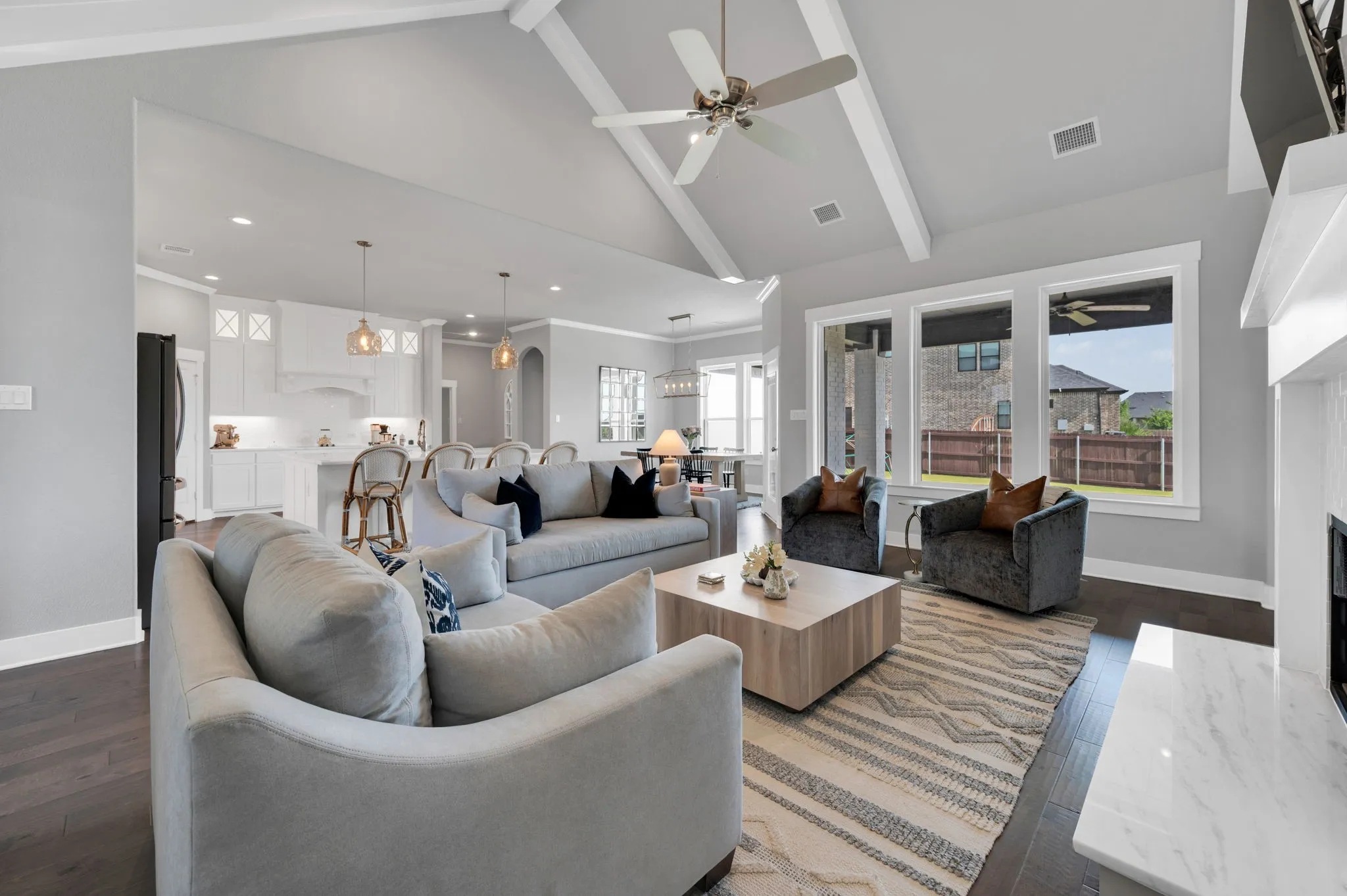 Open-concept living space featuring wood-finish flooring, a vaulted ceiling with exposed beams, and a ceiling fan