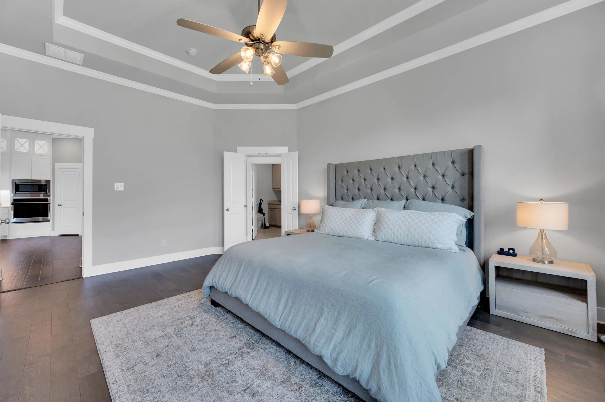 Bedroom featuring a tray ceiling with crown molding, a ceiling fan with integrated lighting, and dark wood-finish flooring