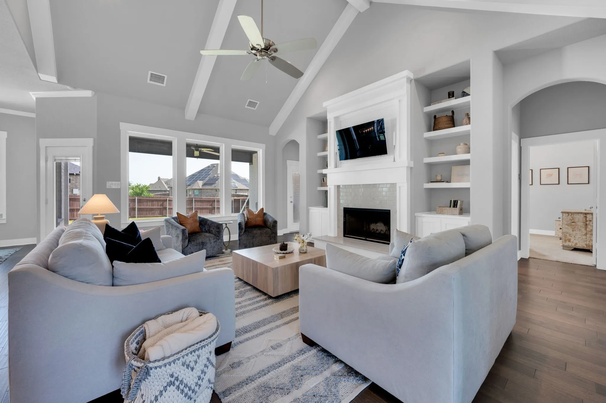 Open-concept living space featuring vaulted ceilings with exposed beams, wood-finish flooring, a built-in fireplace with a tile surround and white mantel, and integrated shelving