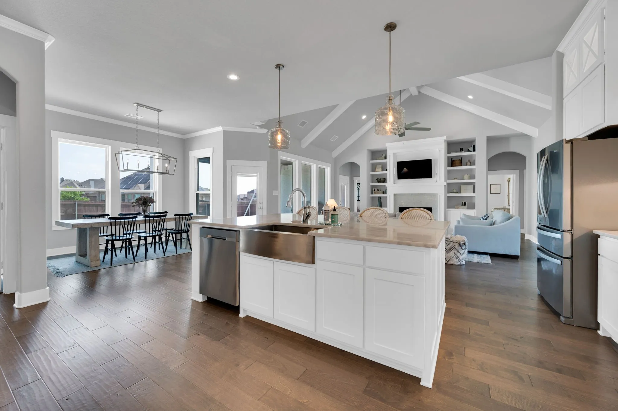 Modern kitchen featuring extensive white cabinetry, a large island with an undermount farmhouse sink, stainless steel appliances, wood-finish flooring, and a white subway tile backsplash