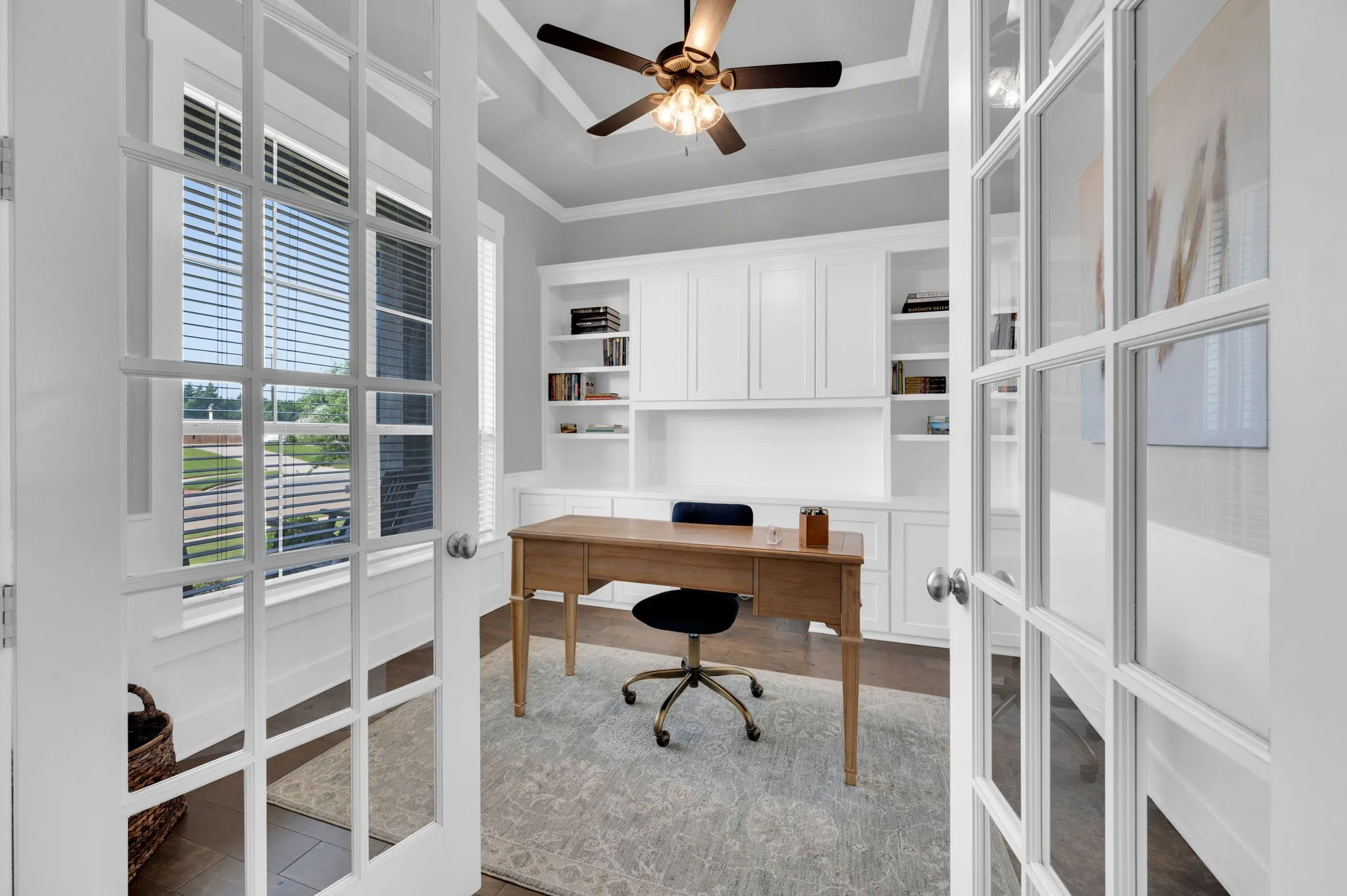French doors opening to a dedicated room featuring a tray ceiling with a ceiling fan, built-in cabinetry, and a large window