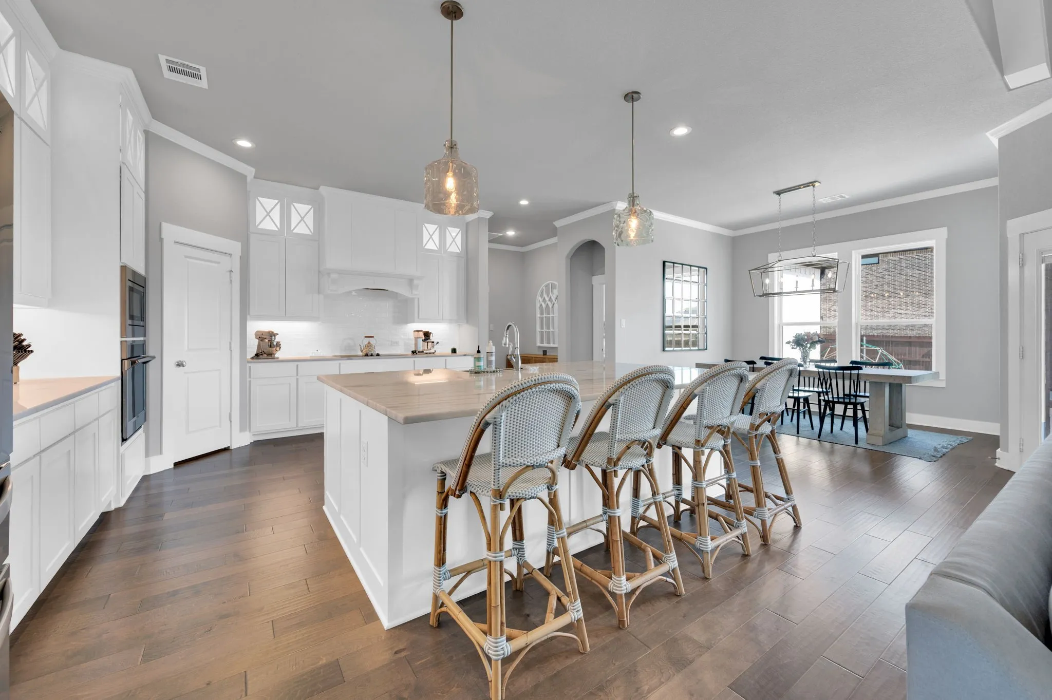 Bright kitchen featuring white cabinetry, wood-finish flooring, a central island with countertop seating, stainless steel double ovens, and a subway tile backsplash