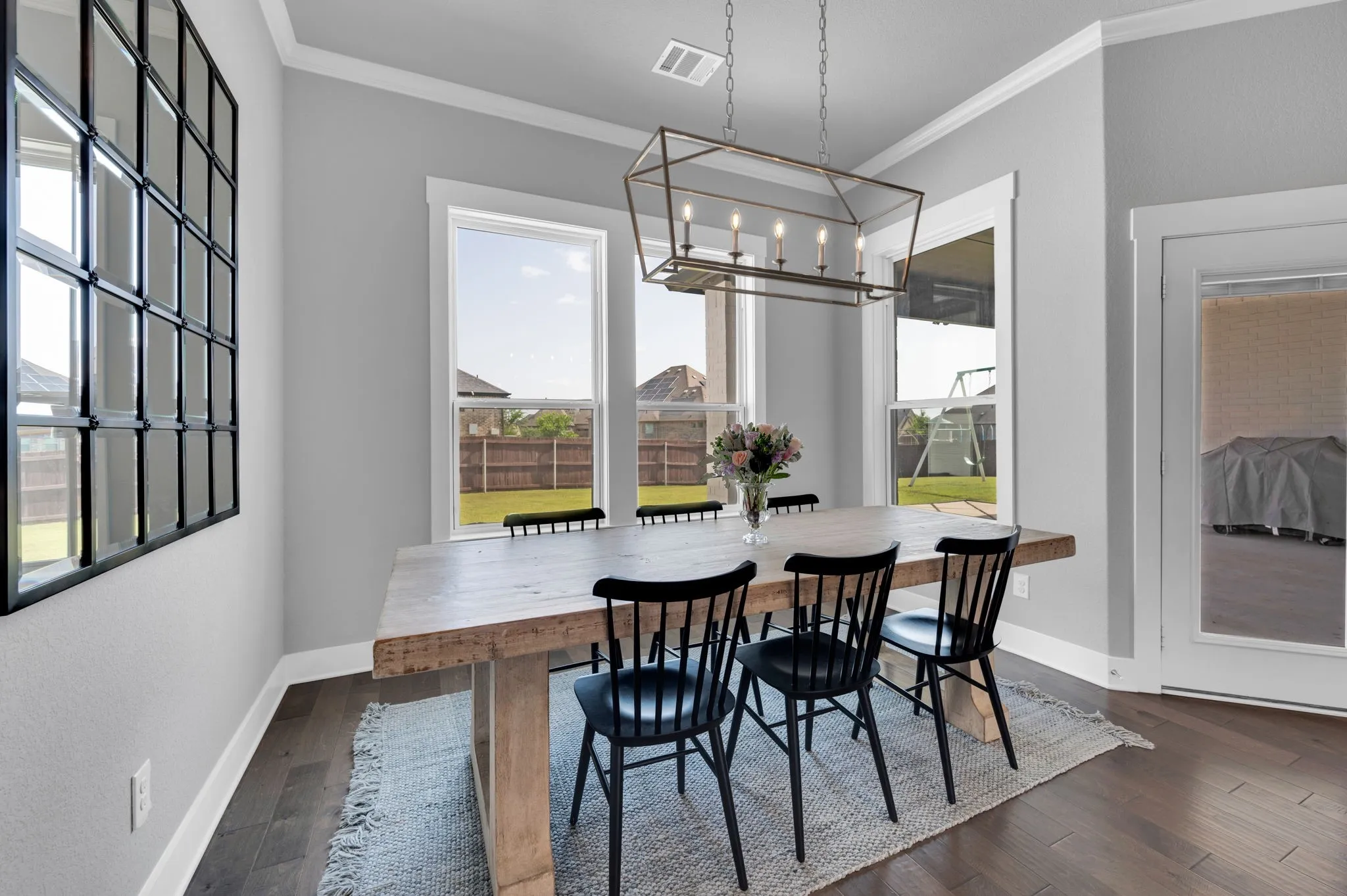 Dining area featuring wood-finish flooring, ample natural light from multiple windows, crown molding, and a contemporary chandelier