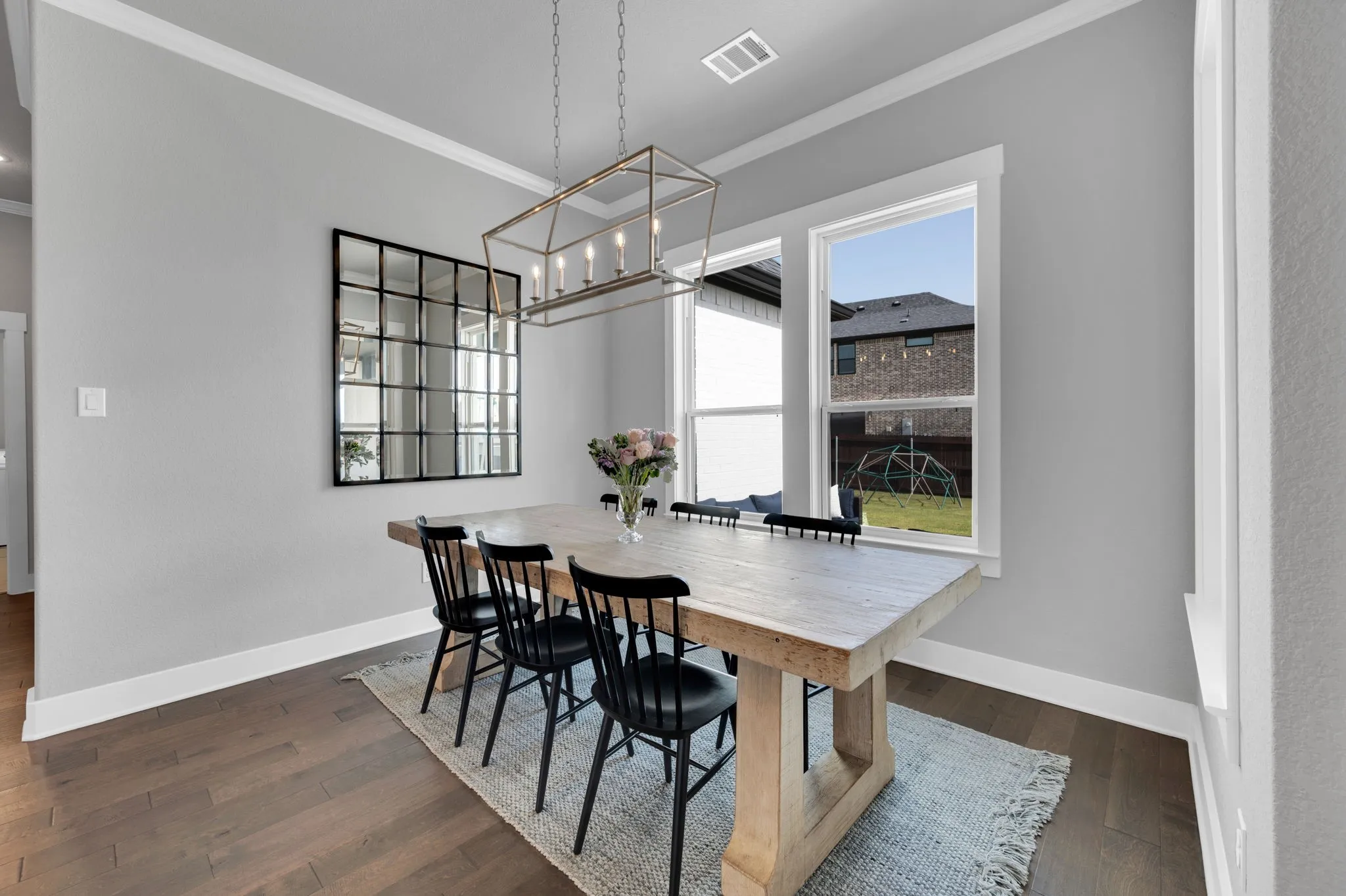 Dining area featuring wood-finish flooring, white crown molding, a multi-pane grid mirror, a linear chandelier, and dual windows