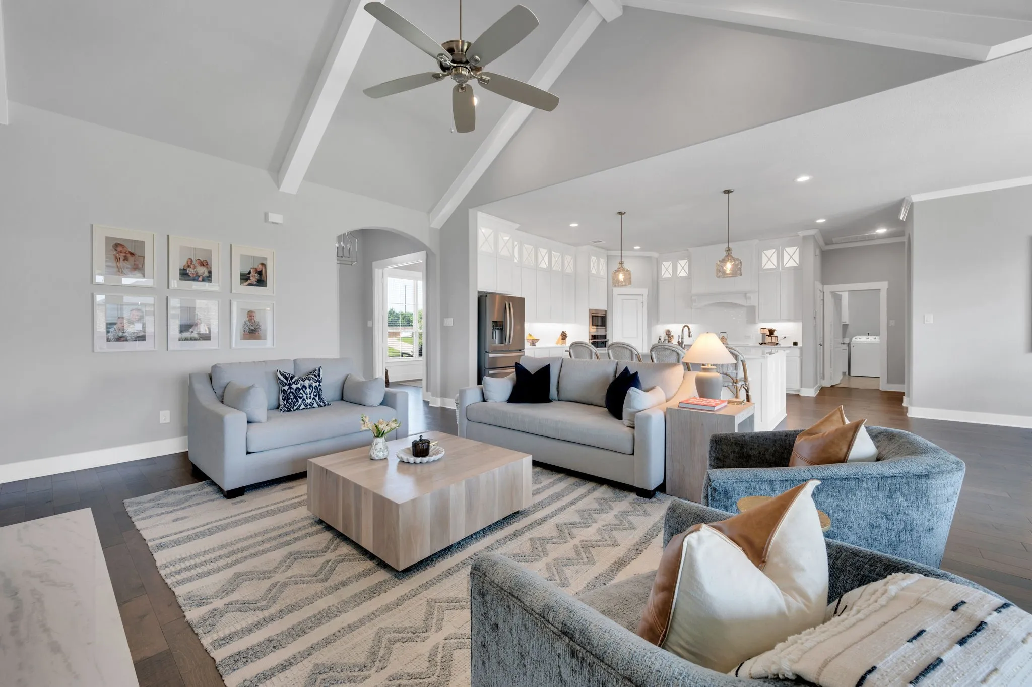 Spacious living area featuring a vaulted ceiling with exposed beams, wood-finish flooring, and an integrated kitchen with pendant lighting