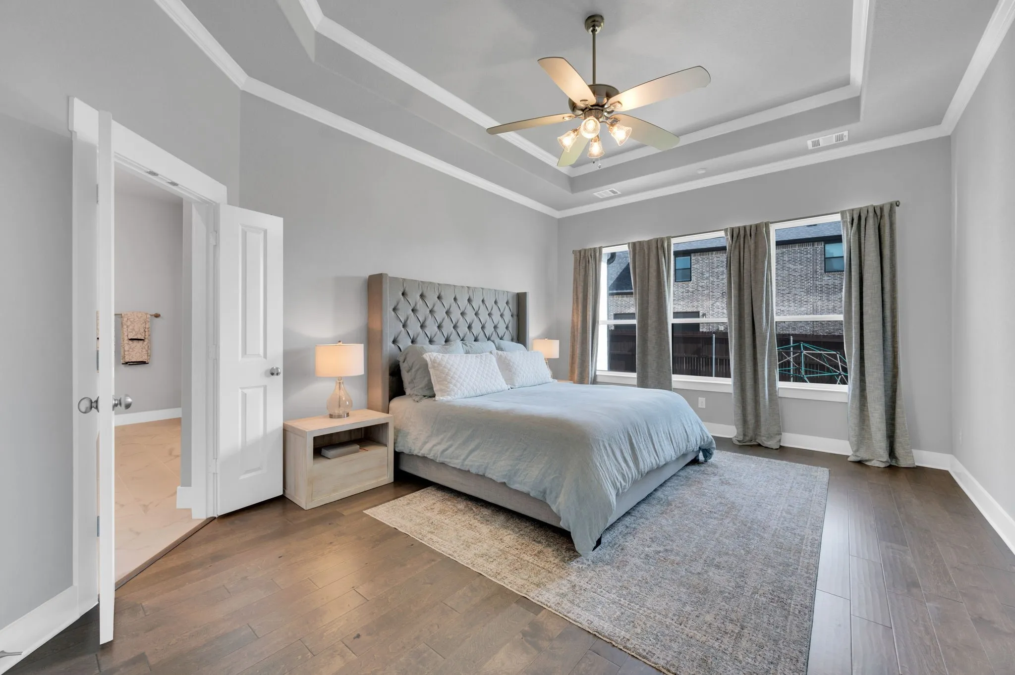 Spacious room featuring rich wood-finish flooring, a tiered tray ceiling with crown molding, and three large windows