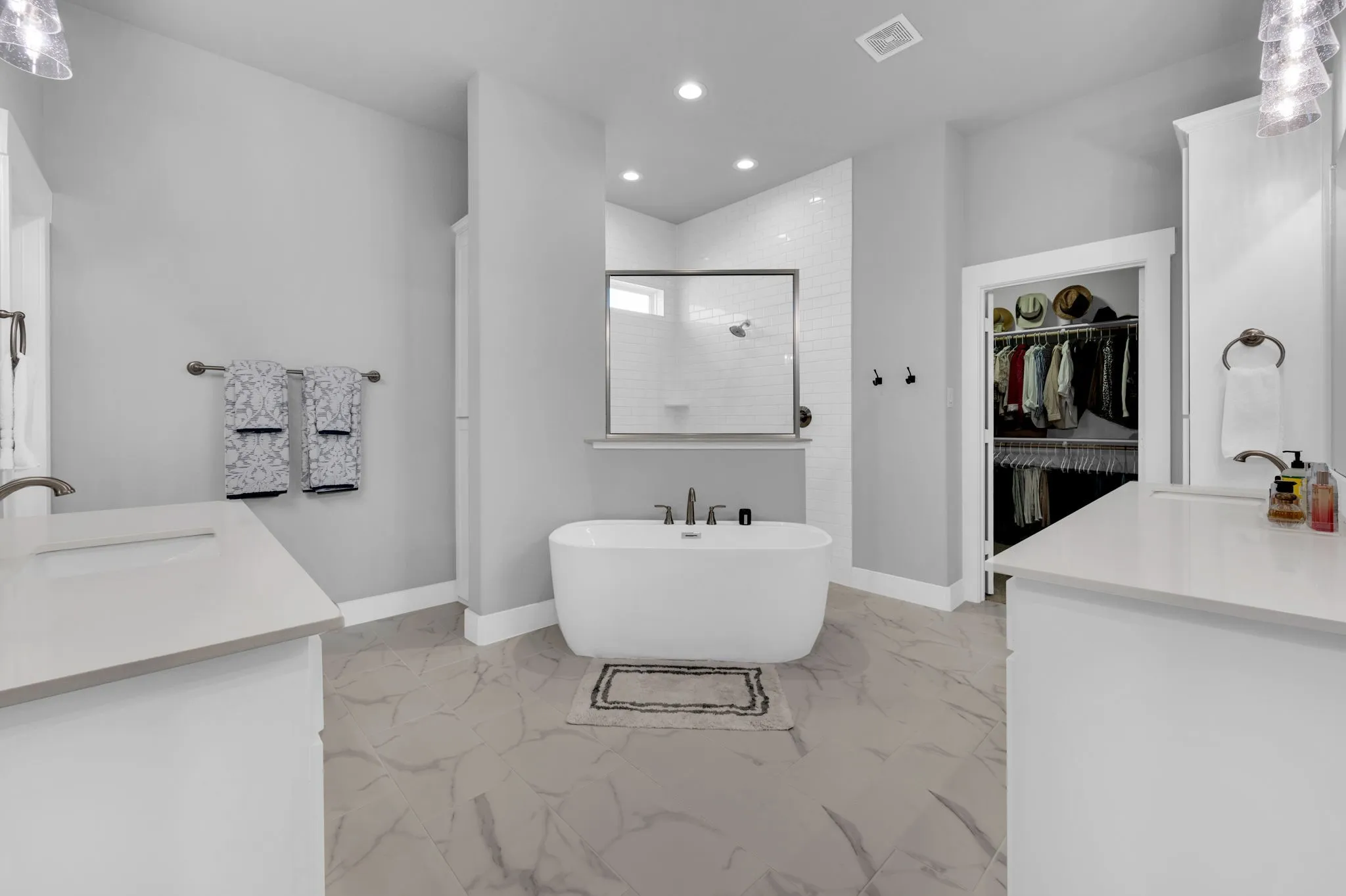 Bathroom featuring a freestanding tub with brushed nickel fixtures, a glass-enclosed shower with subway tile surround, a double vanity with white cabinetry and a light-colored countertop, and large format floor tiling