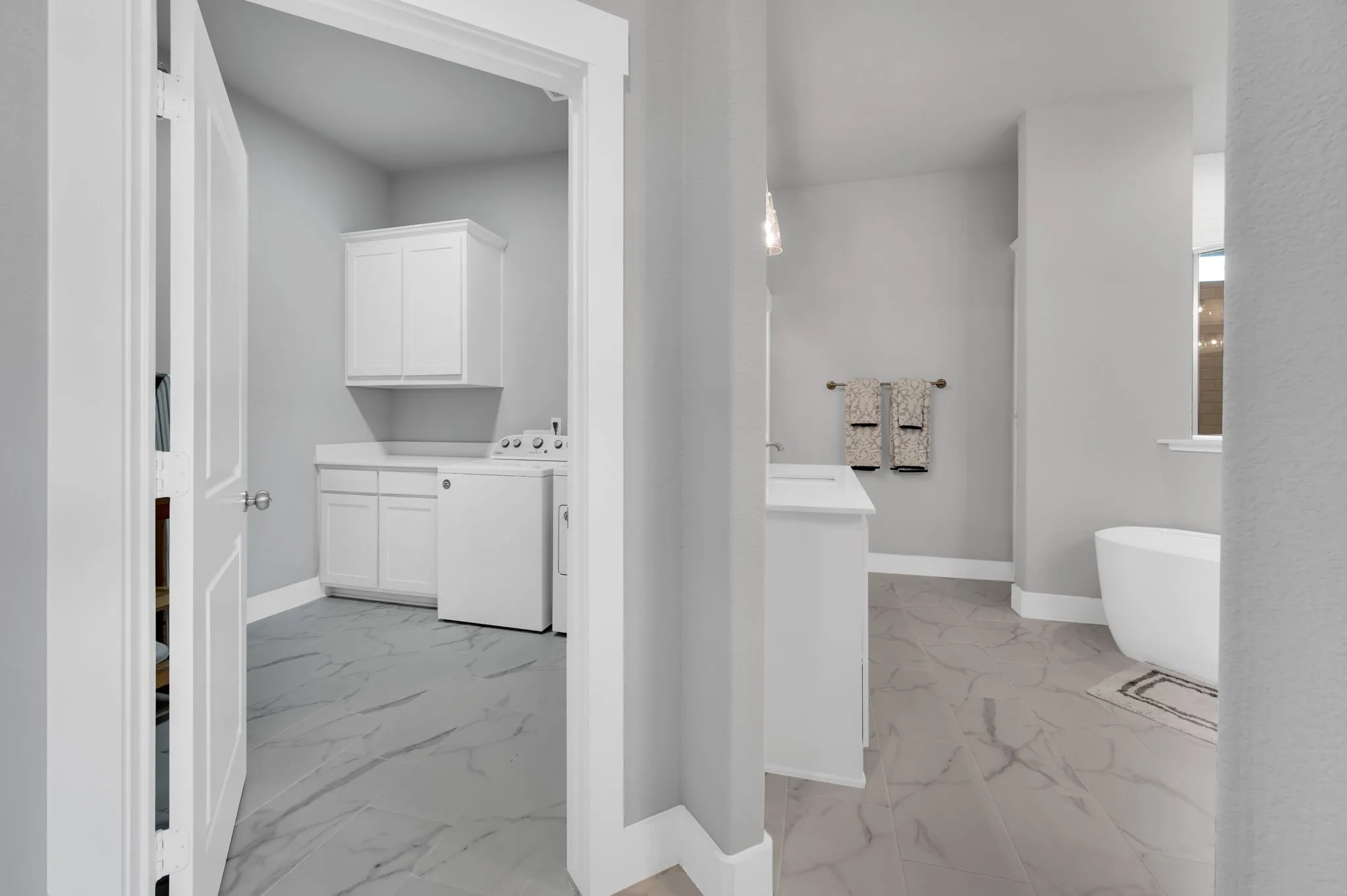 Dedicated laundry space with entrance from primary bathroom featuring white upper cabinetry, lower cabinetry with a light-toned countertop, and light-colored flooring with a subtle veining pattern