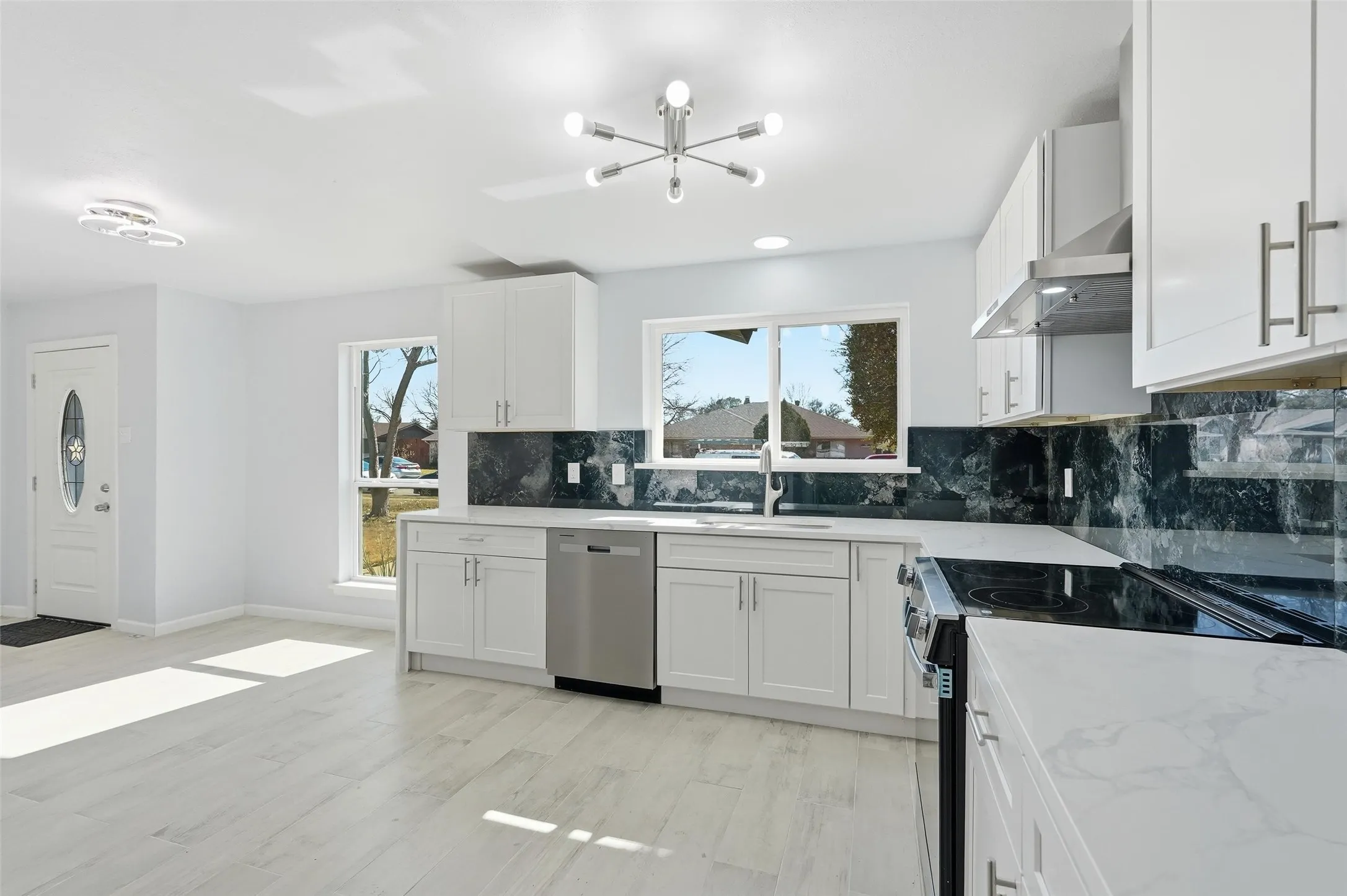 Open-concept kitchen featuring white shaker cabinetry, light-toned wood-finish flooring, and a striking dark stone backsplash