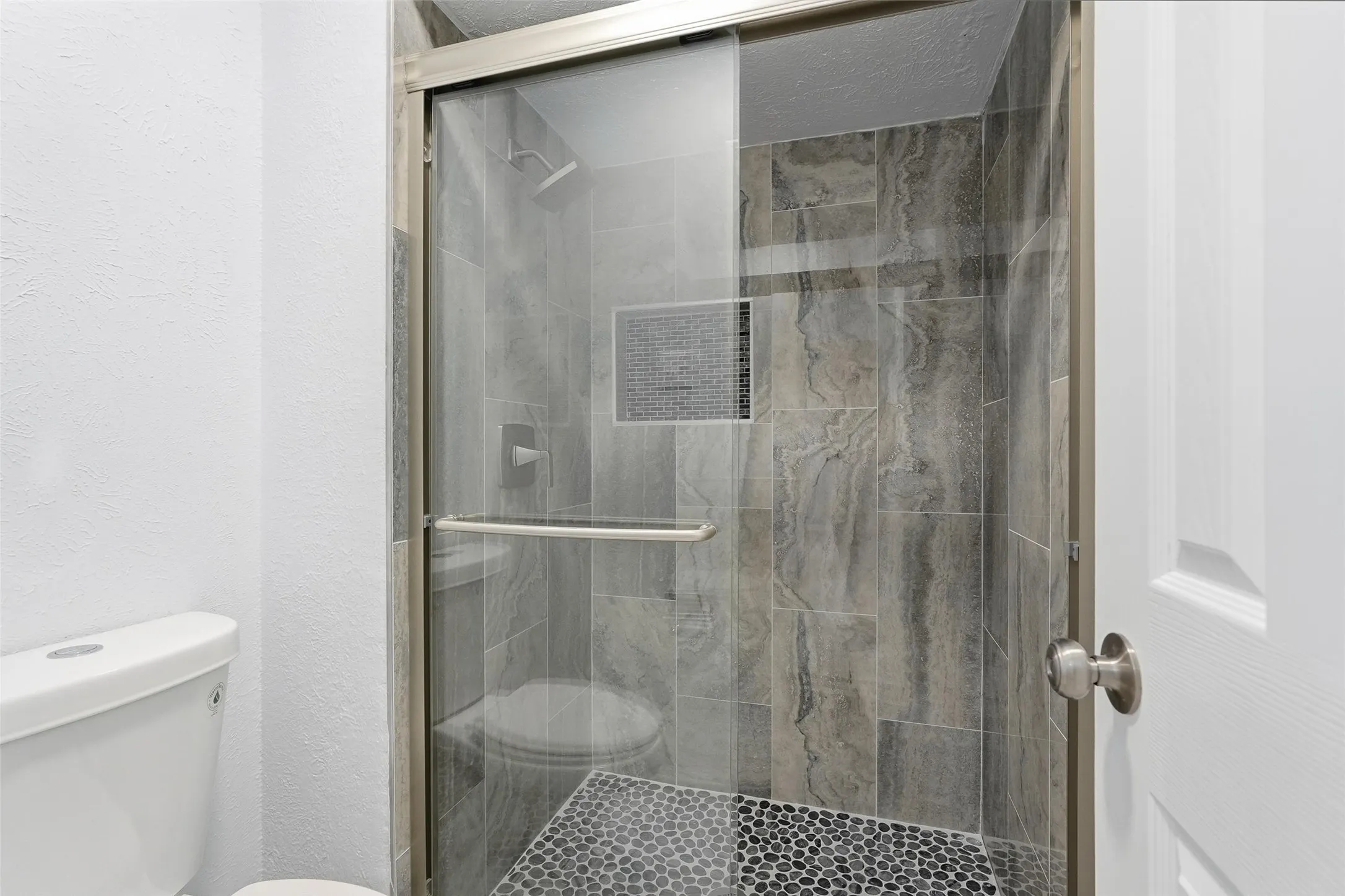 Walk-in shower with a glass enclosure and brushed nickel hardware