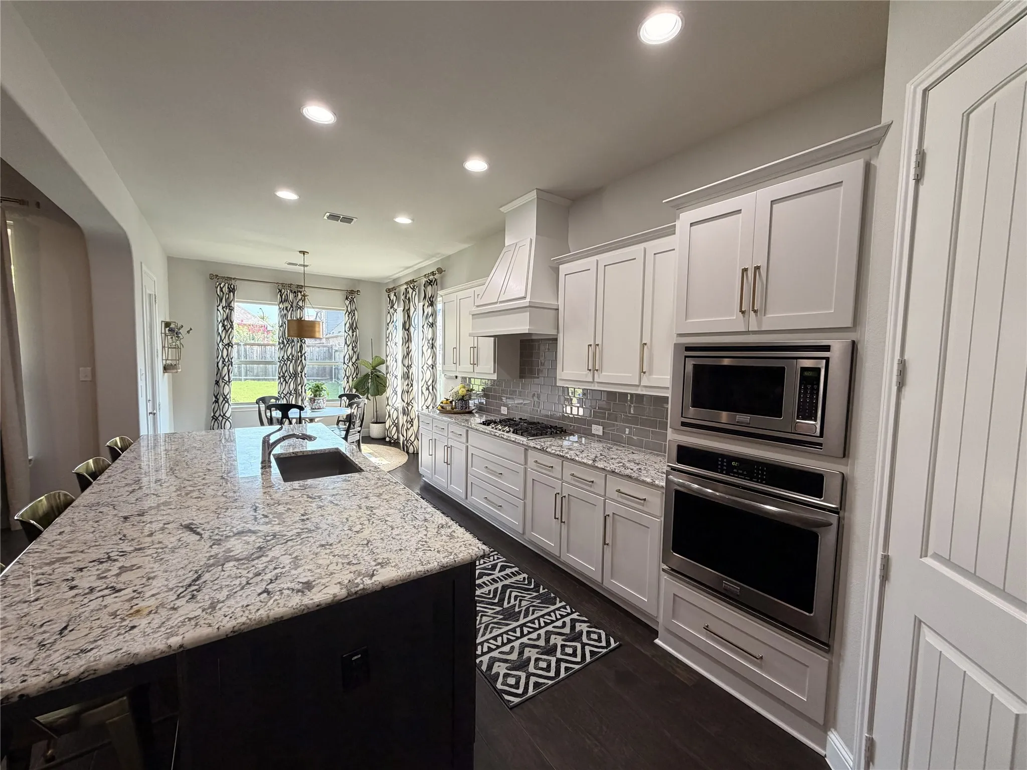 Expansive kitchen featuring a large island with sink, light-toned countertops, white cabinetry, integrated stainless steel appliances, and dark wood-finish flooring