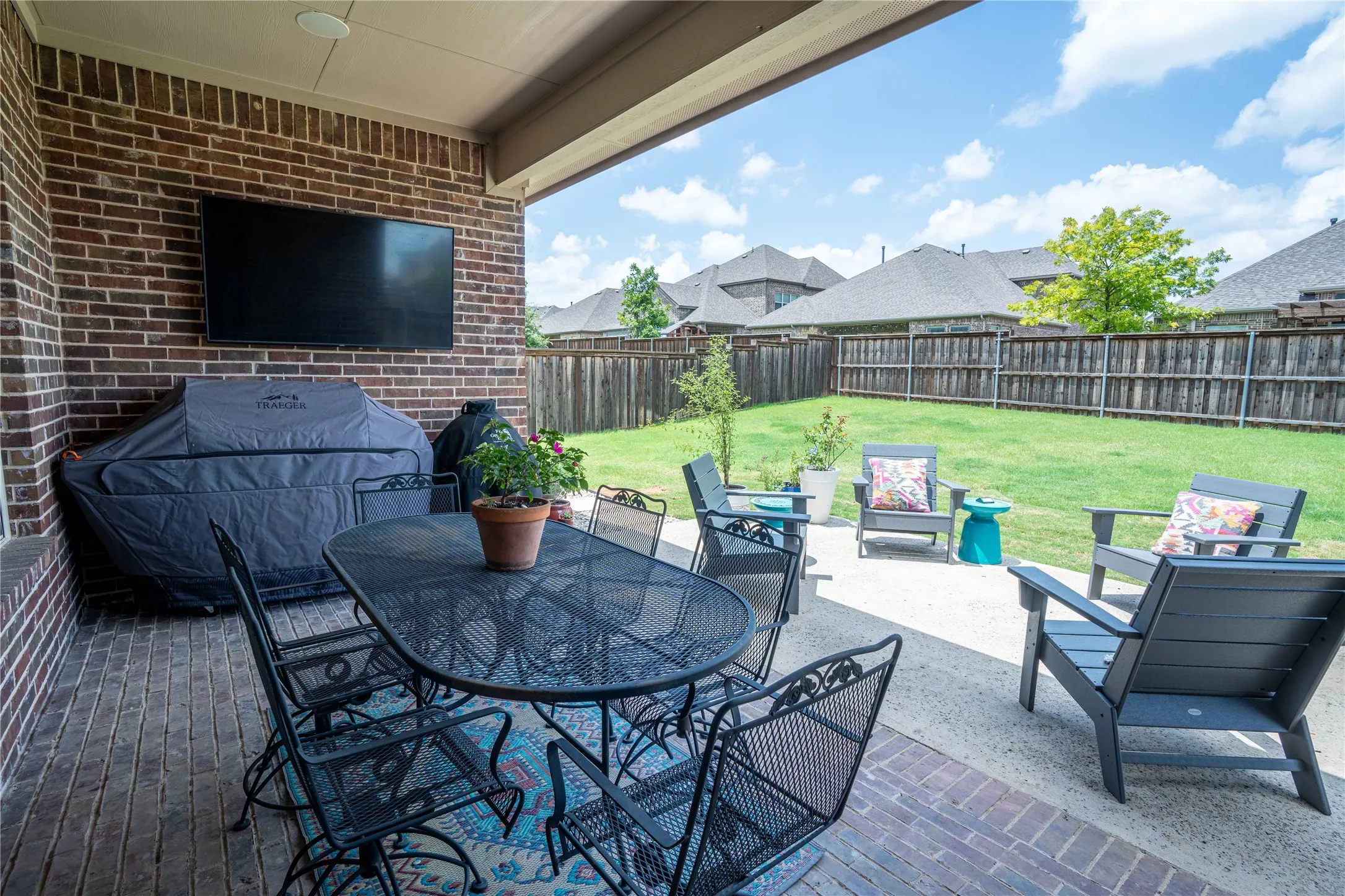 Covered brick patio featuring a mounted outdoor television, brick wall, and a concrete extension