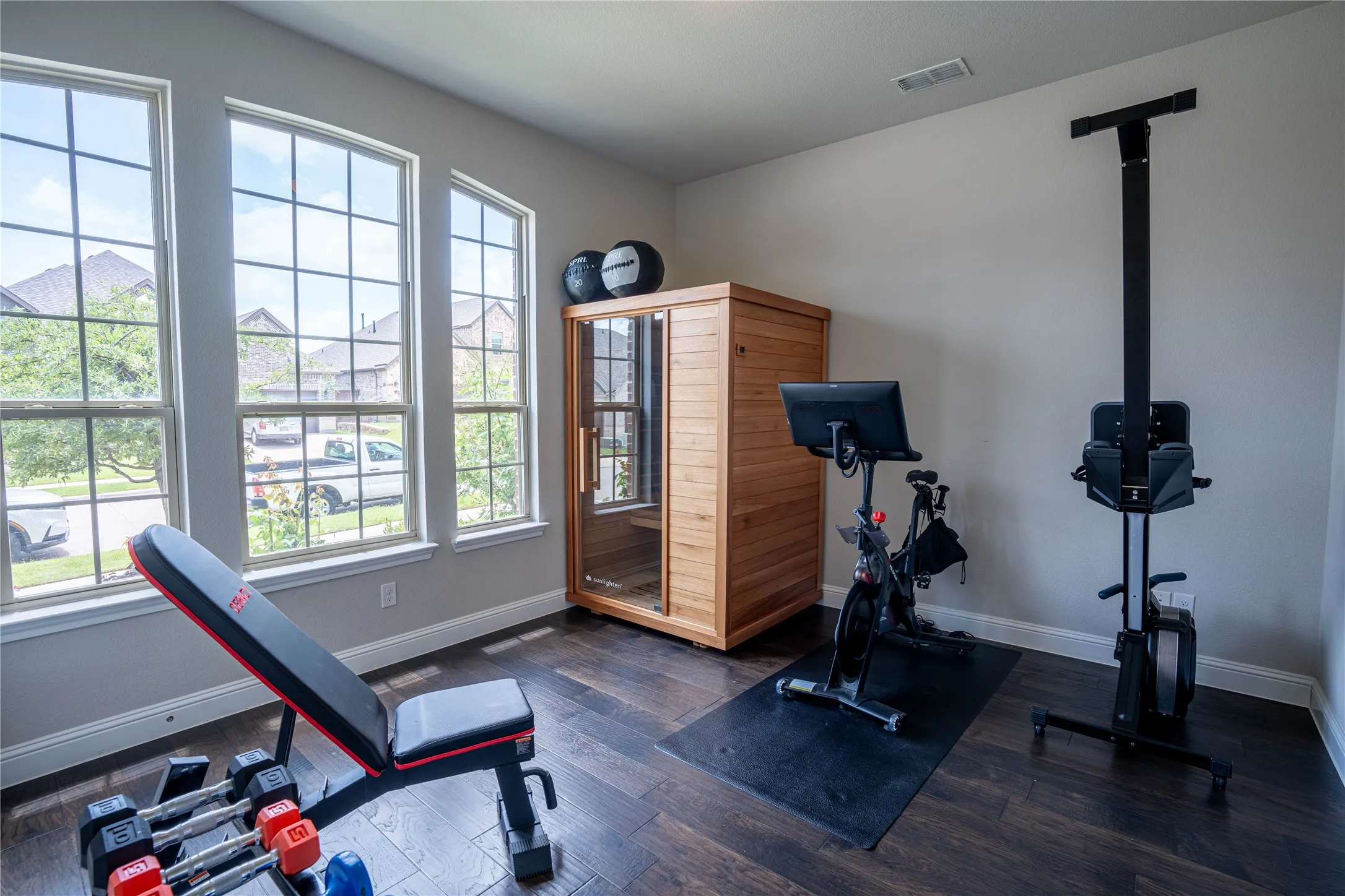 Versatile room featuring dark wood-finish flooring, light-toned walls, and three prominent arched windows with grid patterns
