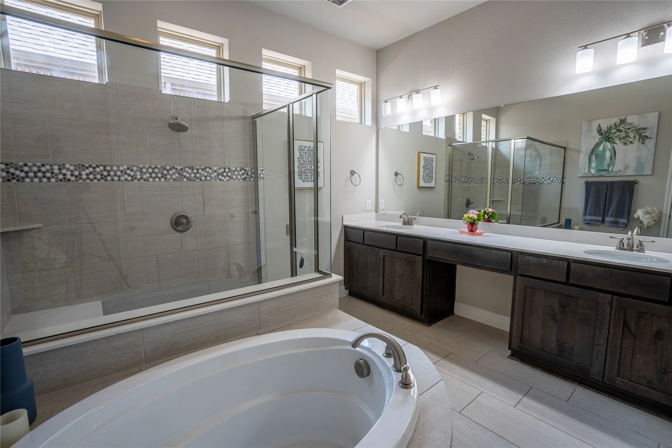 Bathroom featuring a soaking tub, a frameless glass shower enclosure with a rain shower head, dual vanities with white countertops, and wood-finish cabinetry