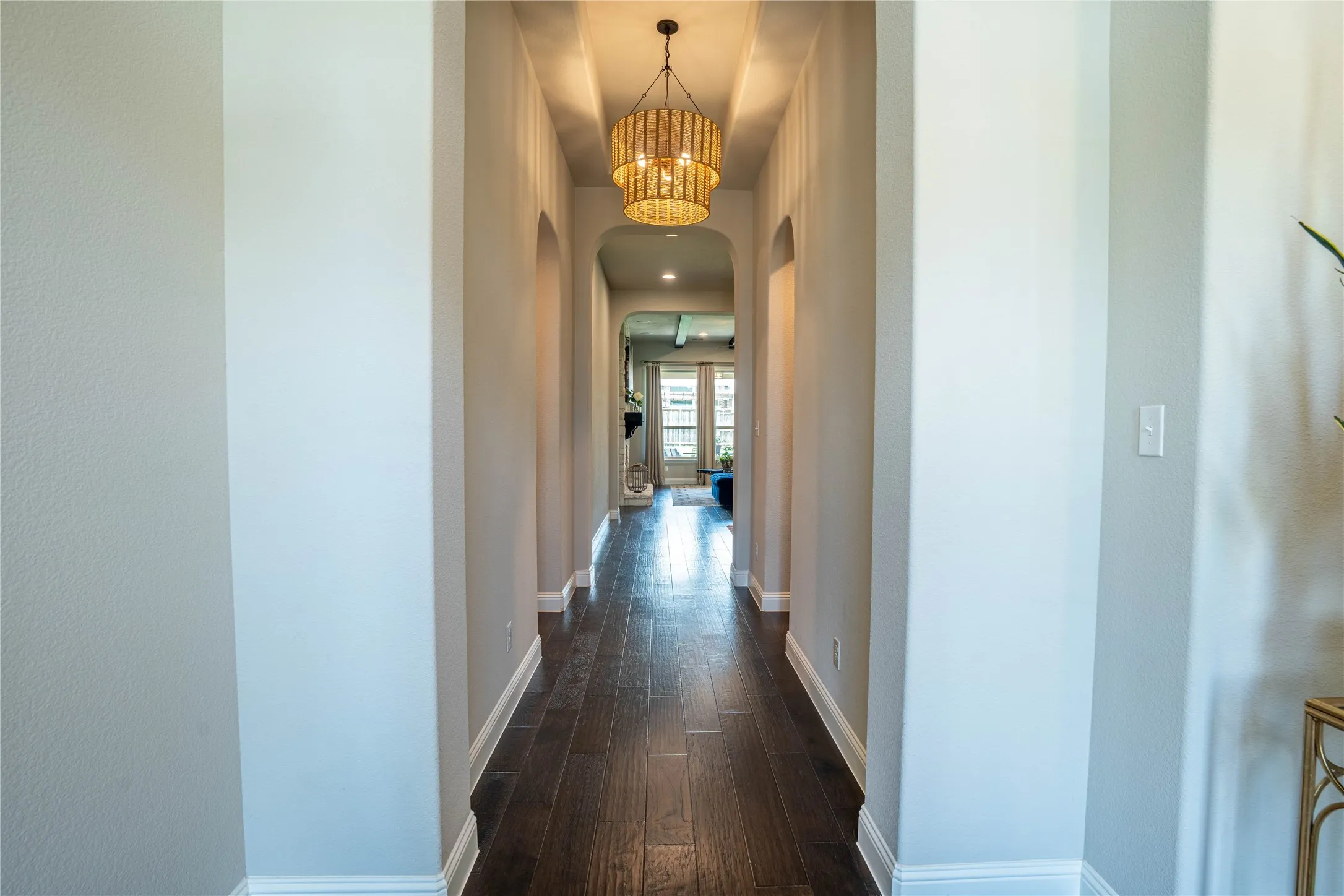 Long hallway featuring dark wood-finish flooring, white baseboards, and arched doorways