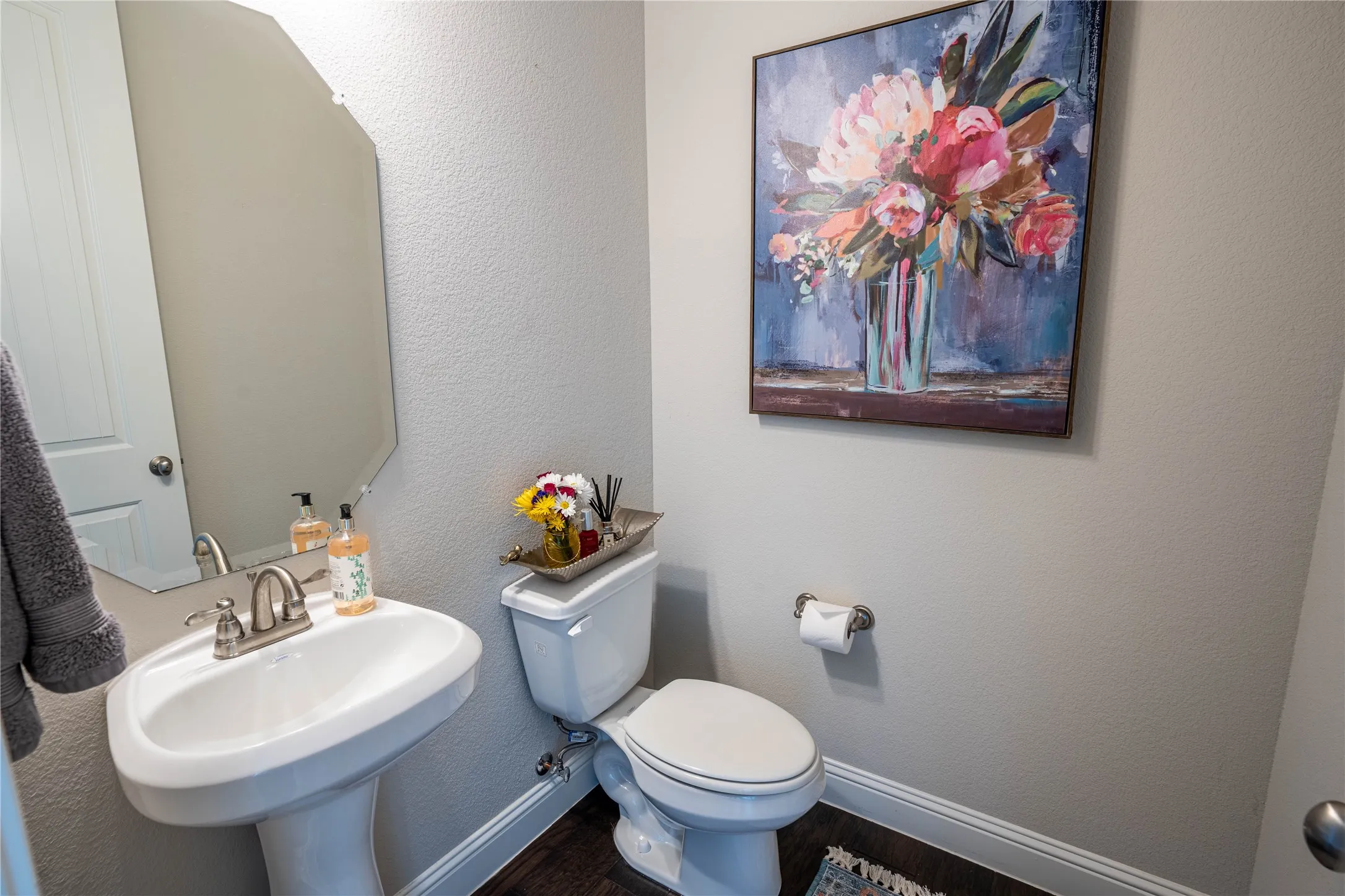 Pedestal sink with a brushed nickel faucet, wall-mounted mirror, and wood-finish flooring