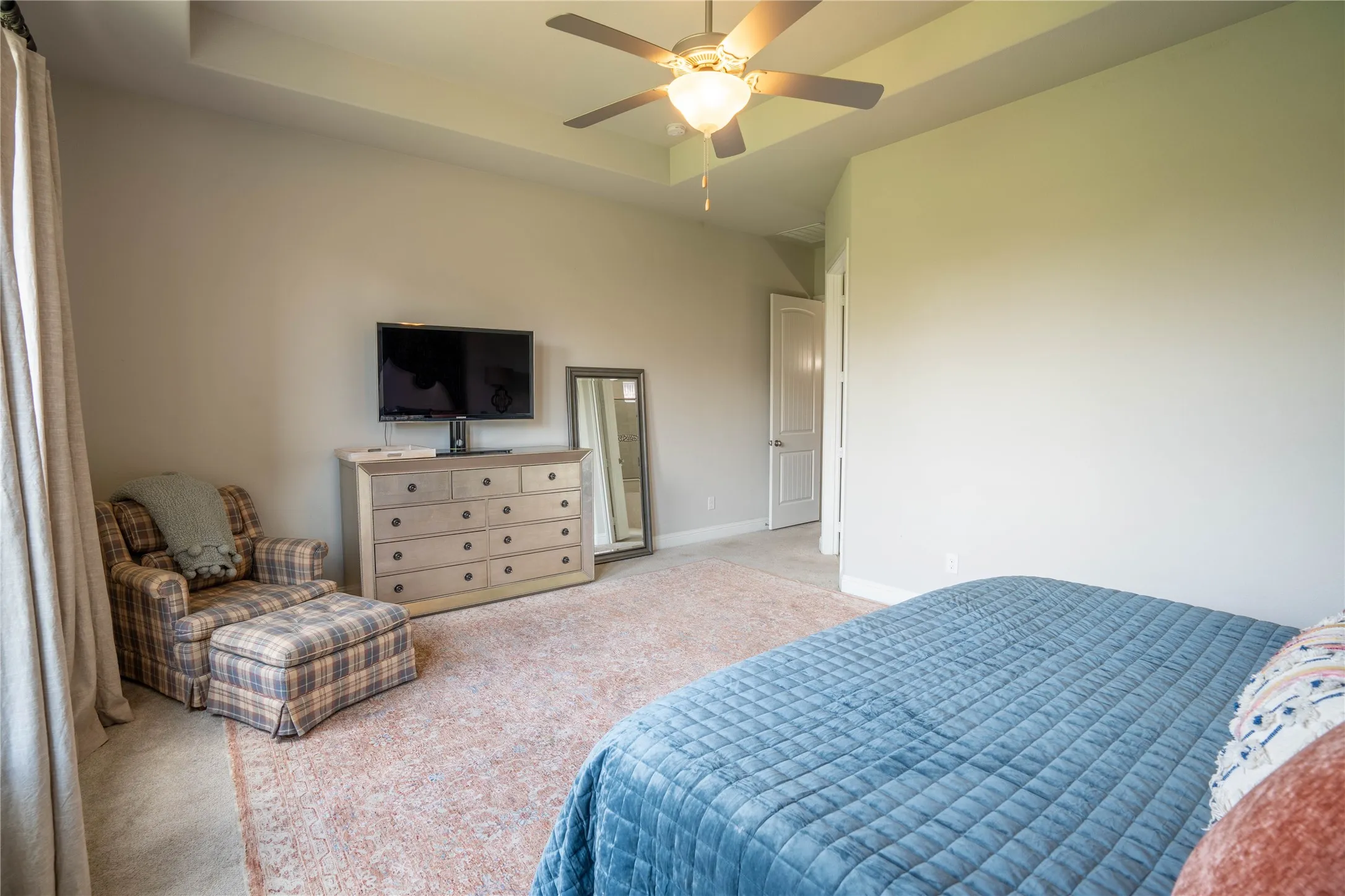Spacious bedroom featuring a tray ceiling, ceiling fan with light fixture, light-colored walls, and a doorway