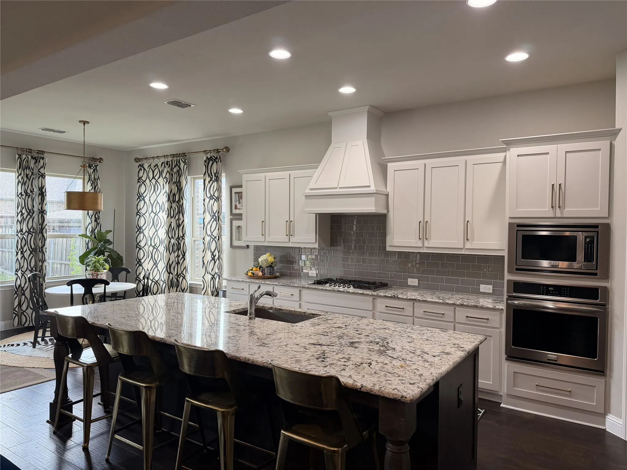 Spacious kitchen featuring an oversized island with seating, white shaker cabinetry, built-in stainless steel appliances, a tile backsplash, and dark wood-finish flooring