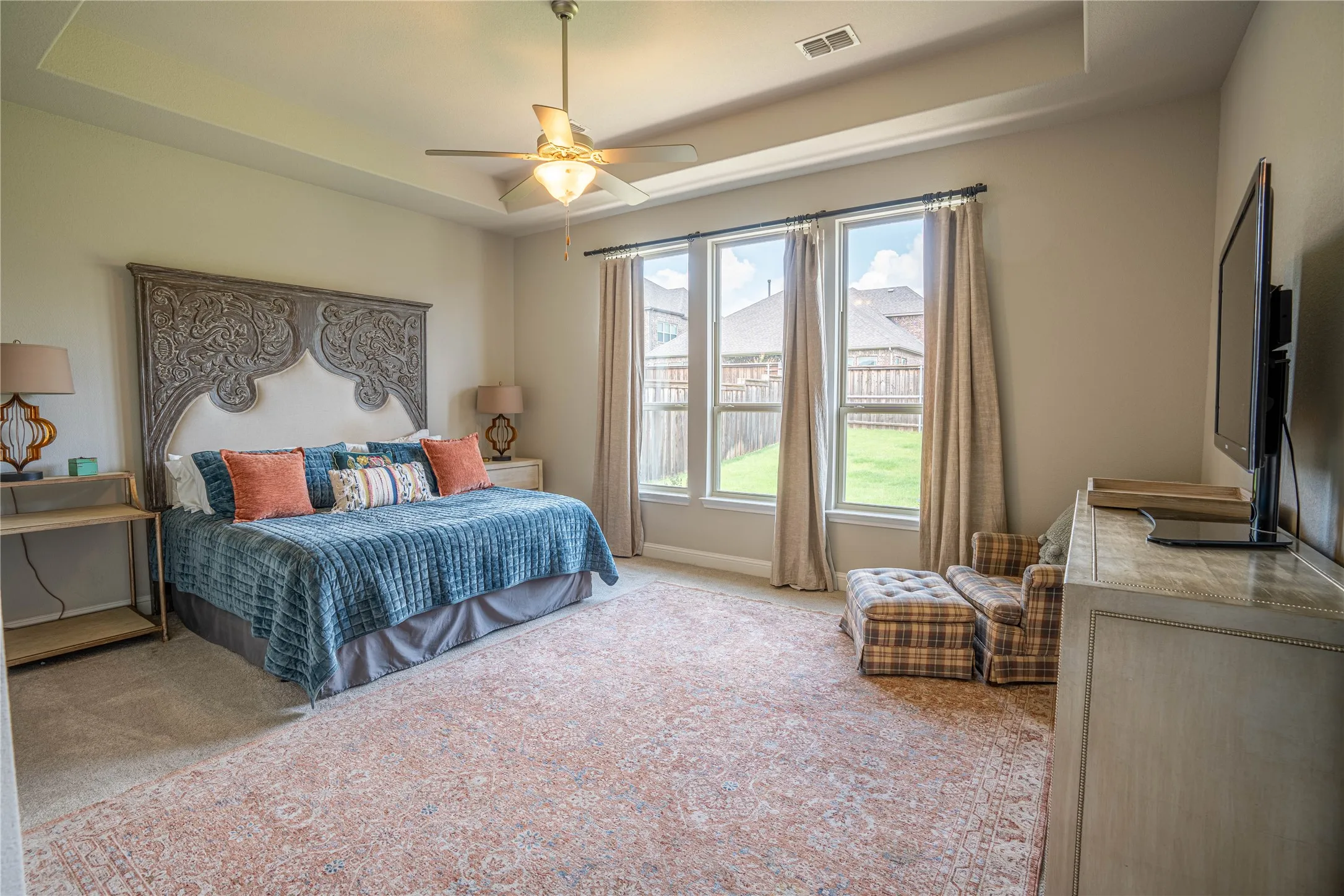 Spacious room featuring a tray ceiling, ceiling fan, and three large windows with curtain rods