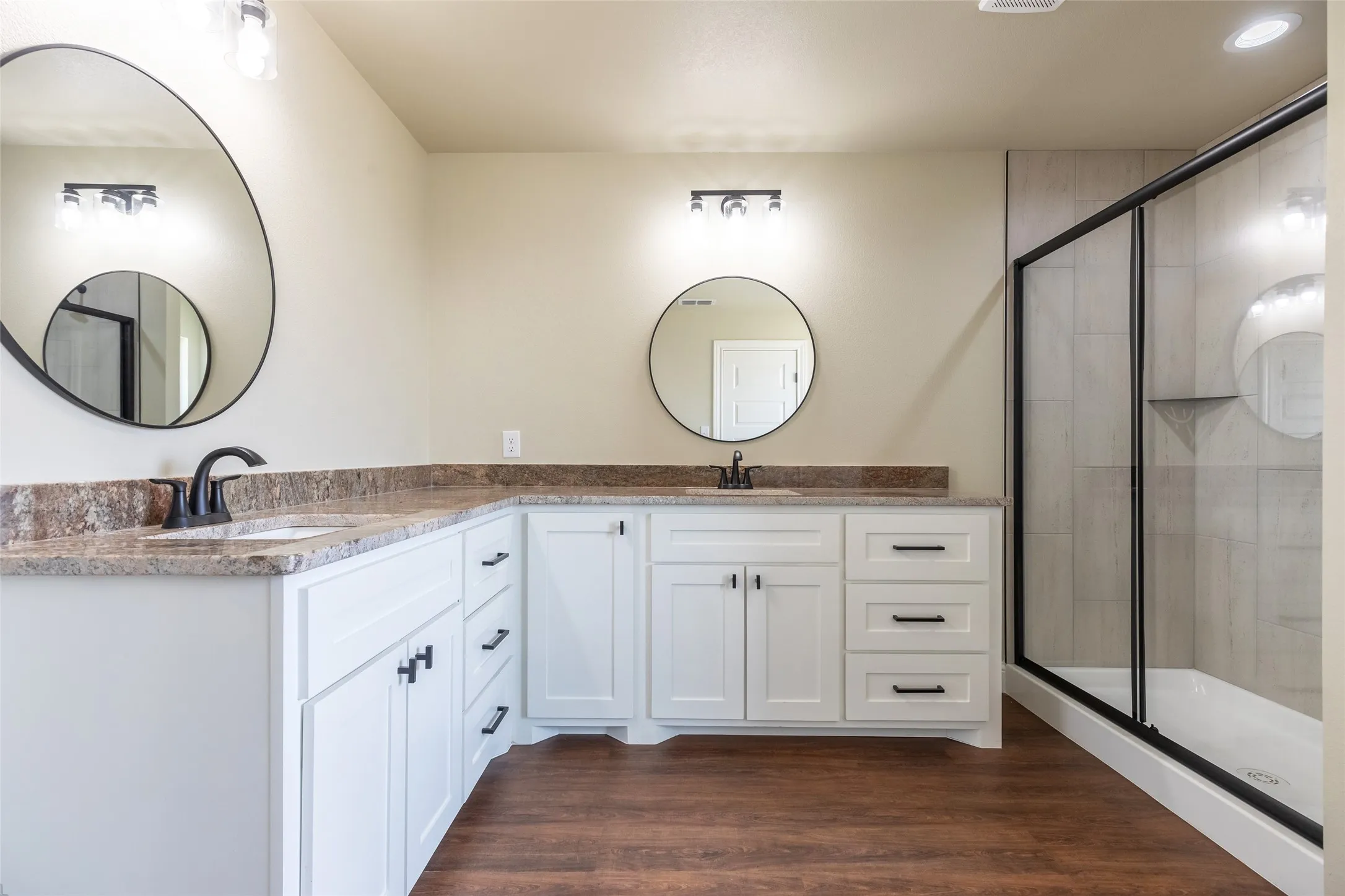 Dual vanity with white cabinetry and dark hardware, complemented by a walk-in shower with clear glass enclosure and tiled walls