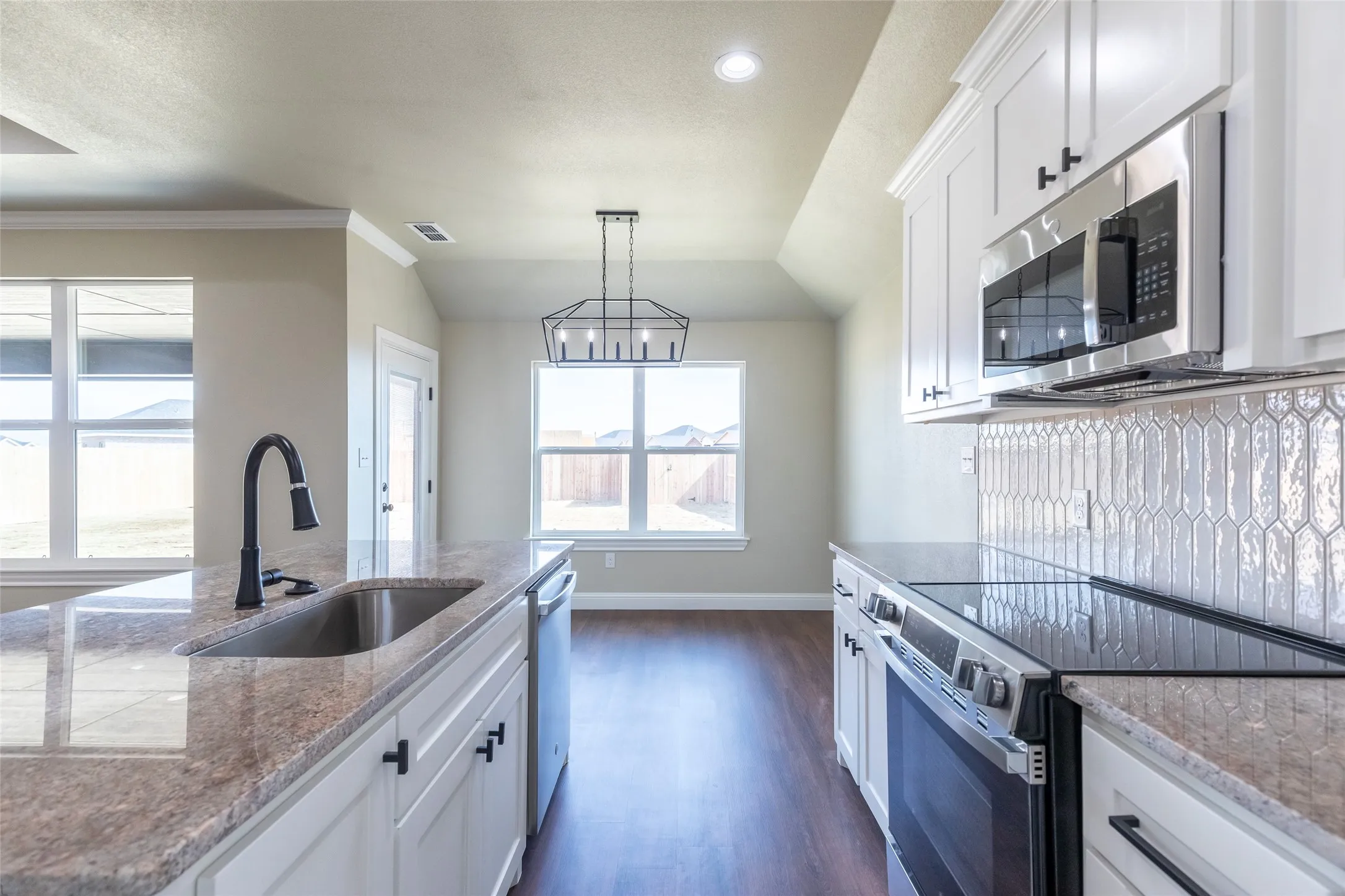 Modern kitchen featuring white cabinetry, granite countertops, stainless steel appliances, a tile backsplash, and wood-finish flooring