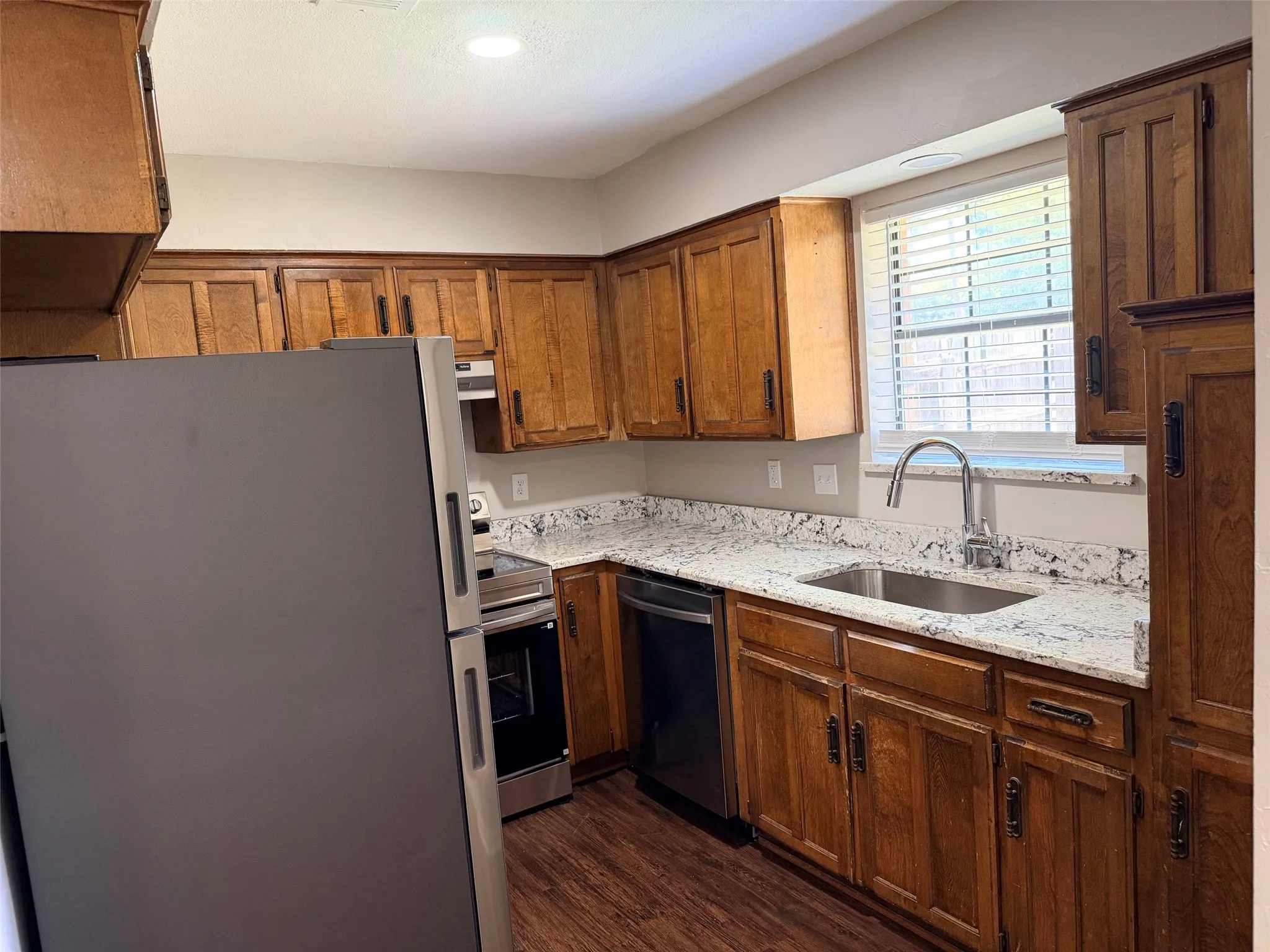 Kitchen featuring wood-finish flooring, light-colored countertops, stainless steel sink with a high-arc faucet, and wood cabinetry throughout