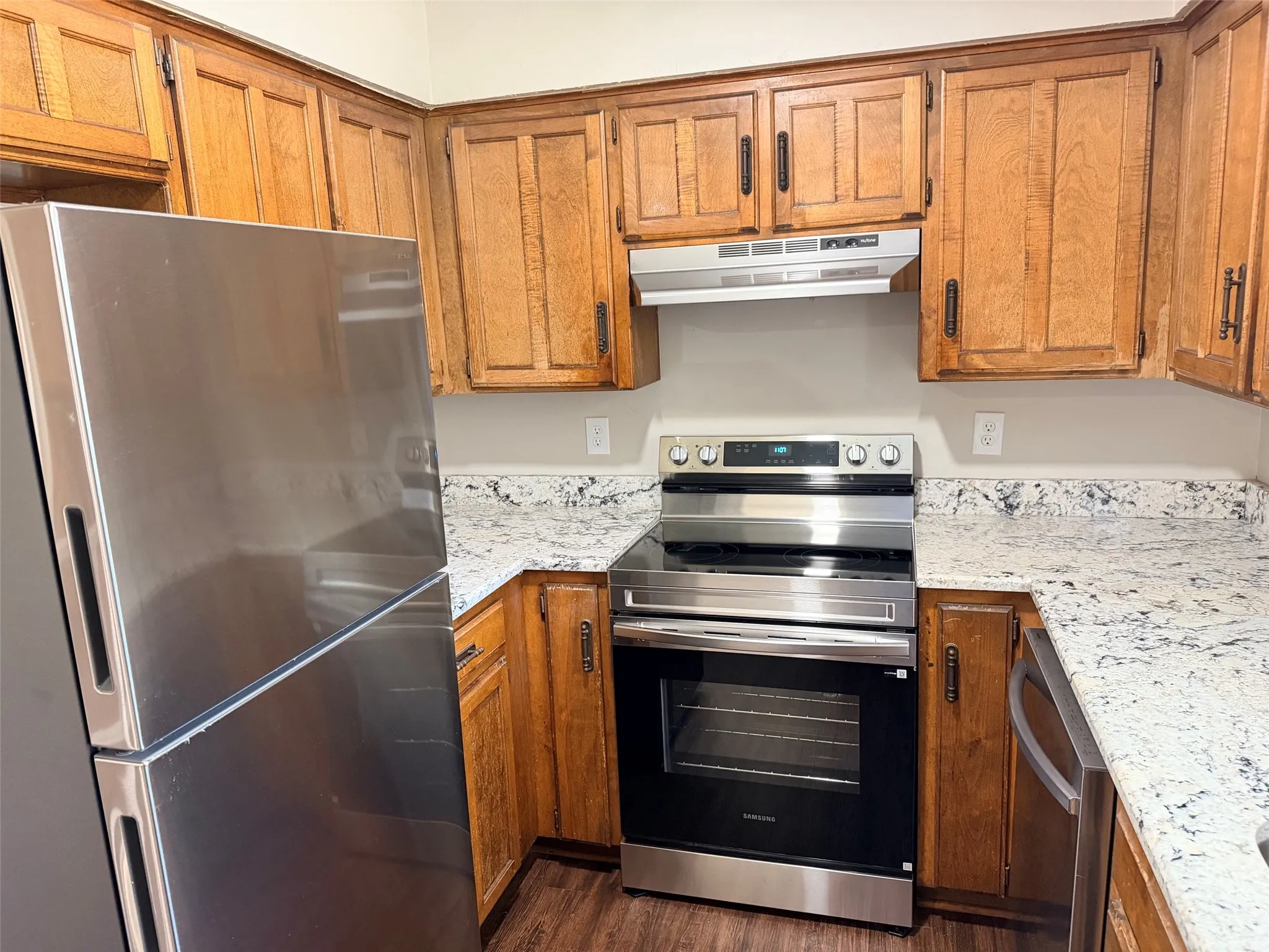 Kitchen featuring wood cabinetry, stainless steel appliances, white patterned countertops, and wood-finish flooring